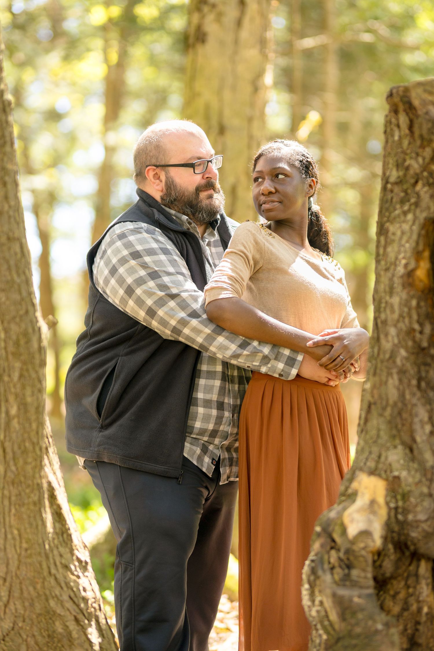 Couple embracing in a sunlit forest wearing casual autumn attire. Ottawa Wedding Photographer