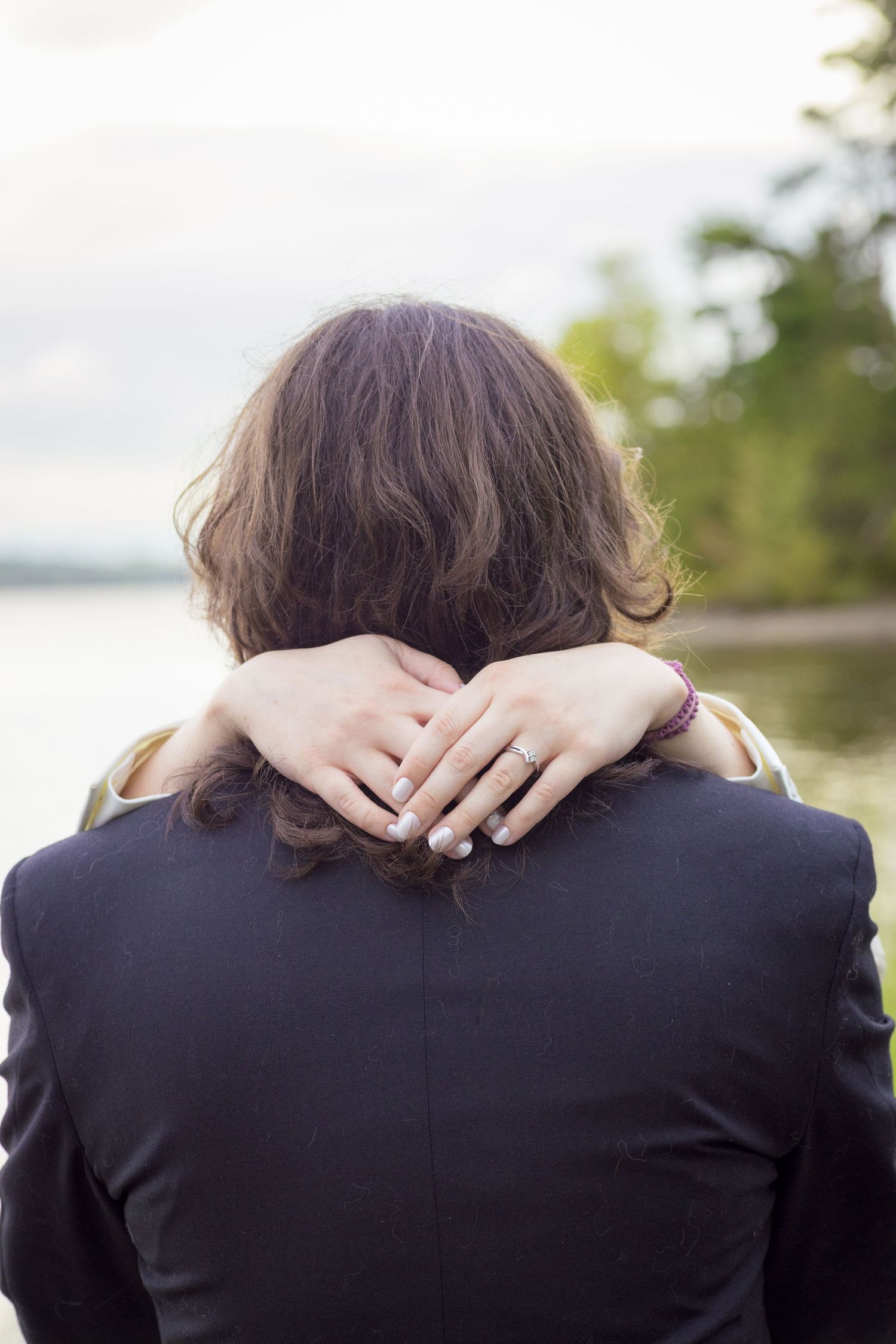 Close up of hands embracing around neck showing wedding rings against dark suit jacket. Ottawa Wedding Photographer