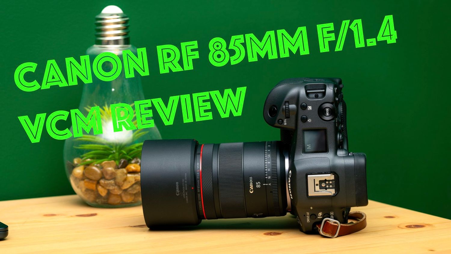 Canon RF 85mm f/1.4 lens displayed with red ring accent against a green background and wooden surface.