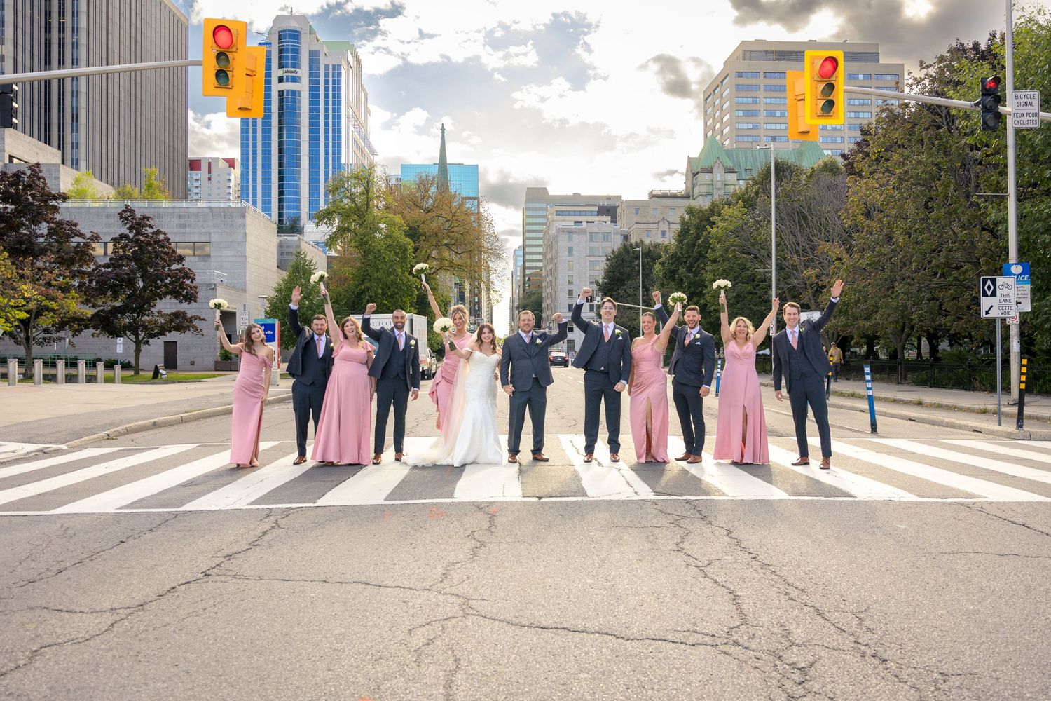 Wedding party poses on a city street with tall buildings and autumn trees in the background. Ottawa Wedding Photographer