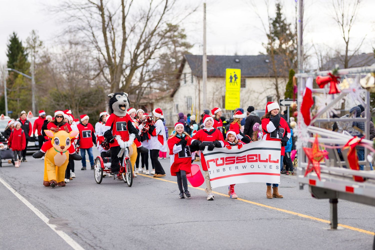 A crowd in red and white Santa outfits gathers for a festive holiday parade or run event on a winter street.