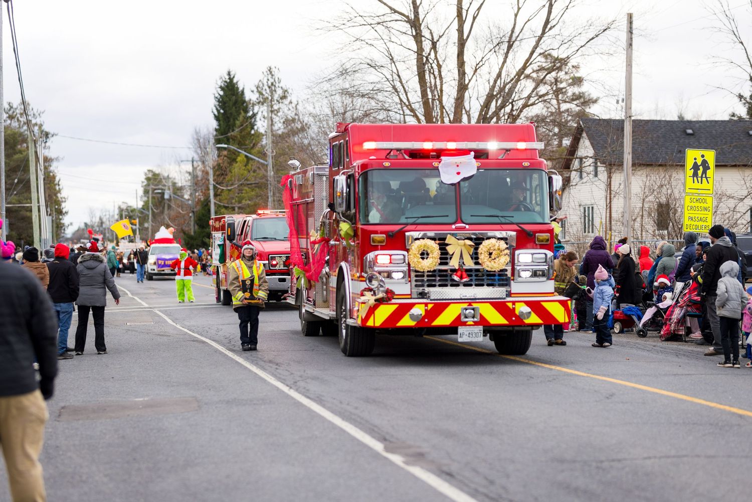 Fire trucks and emergency vehicles line up for a community parade on a residential street with spectators watching.