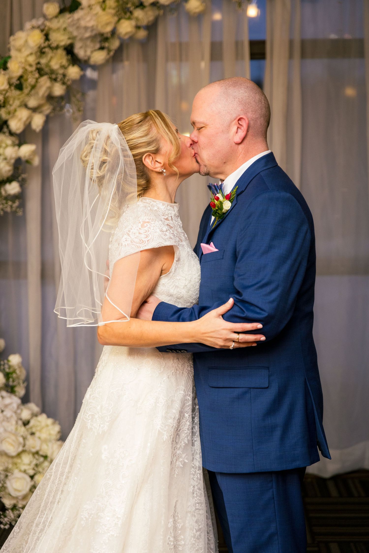 A couple shares their first kiss as newlyweds under a dreamy floral arch, surrounded by winter wedding magic. ❄️💍 | Tim Gowling Photography