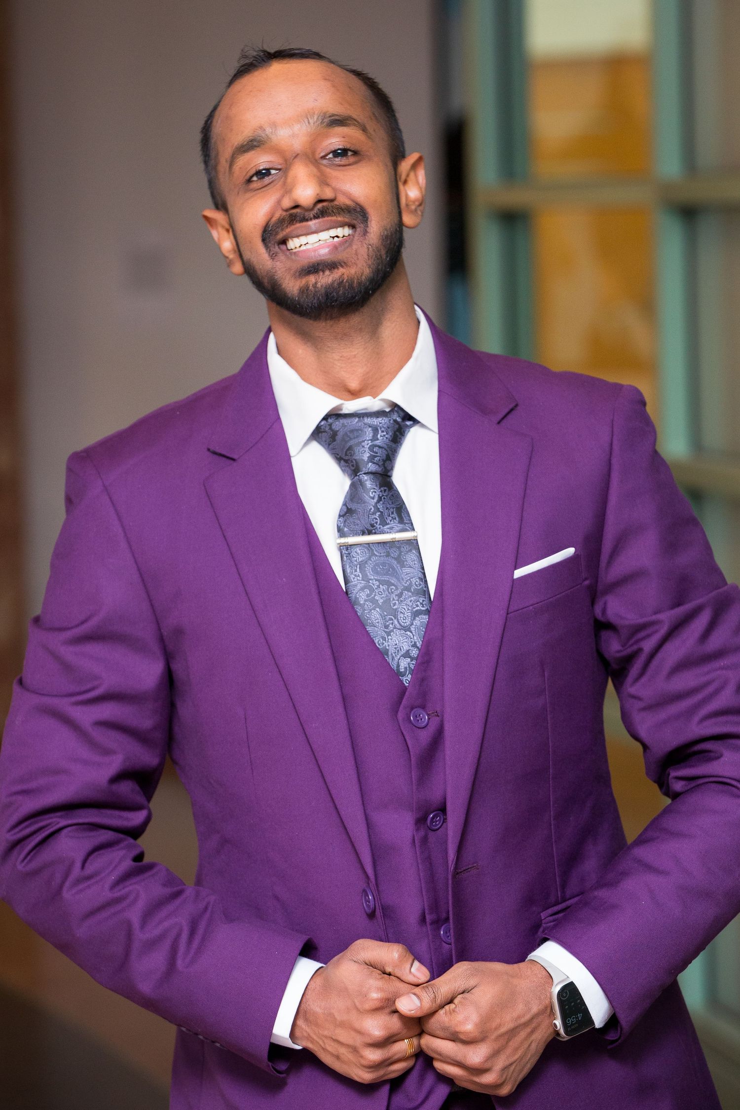 A person wearing a stylish purple three-piece suit and patterned tie smiles at the camera.