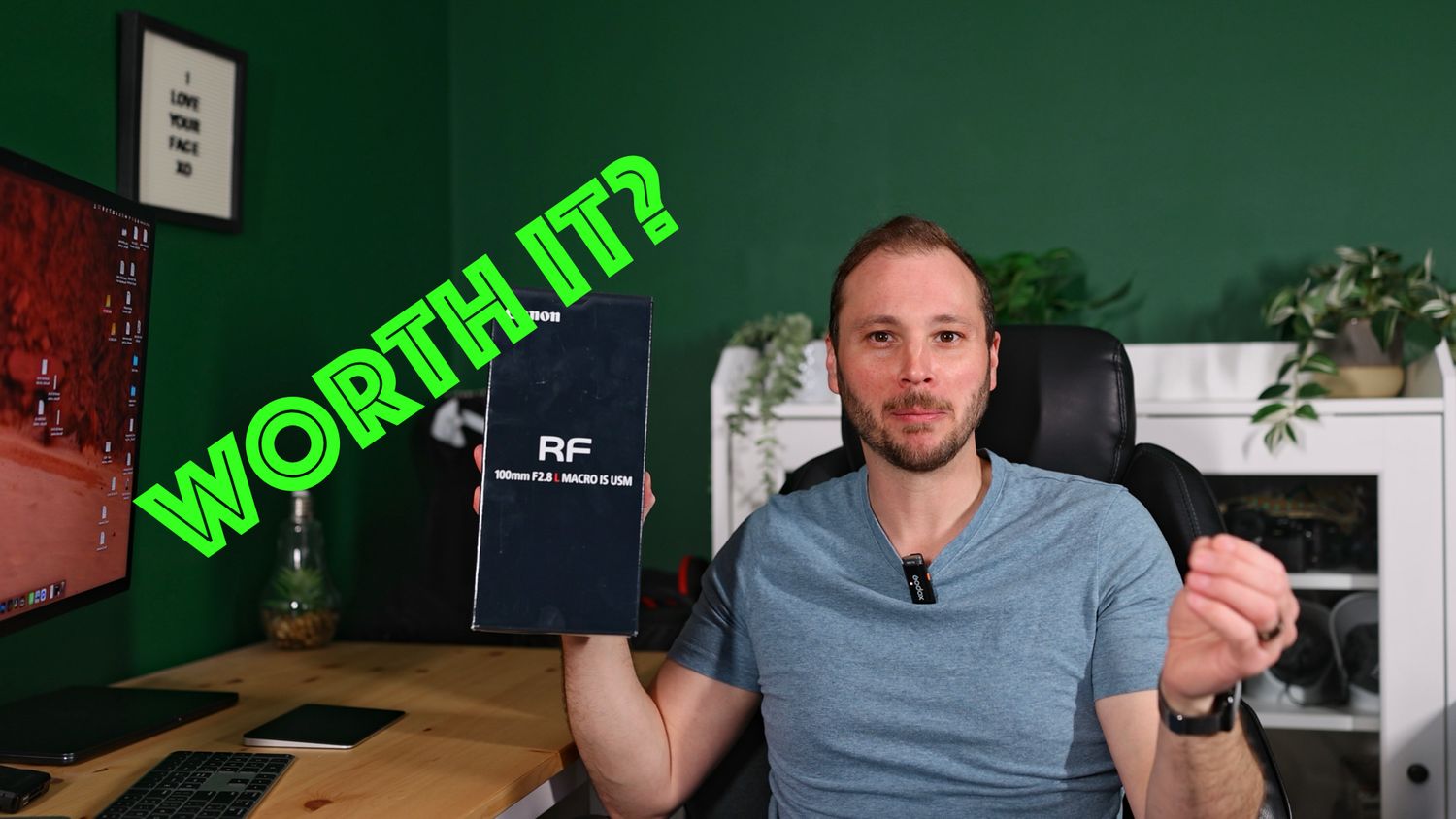 Man holding an RF lens box at a desk asking 'Worth It?' in a green home office setup.
