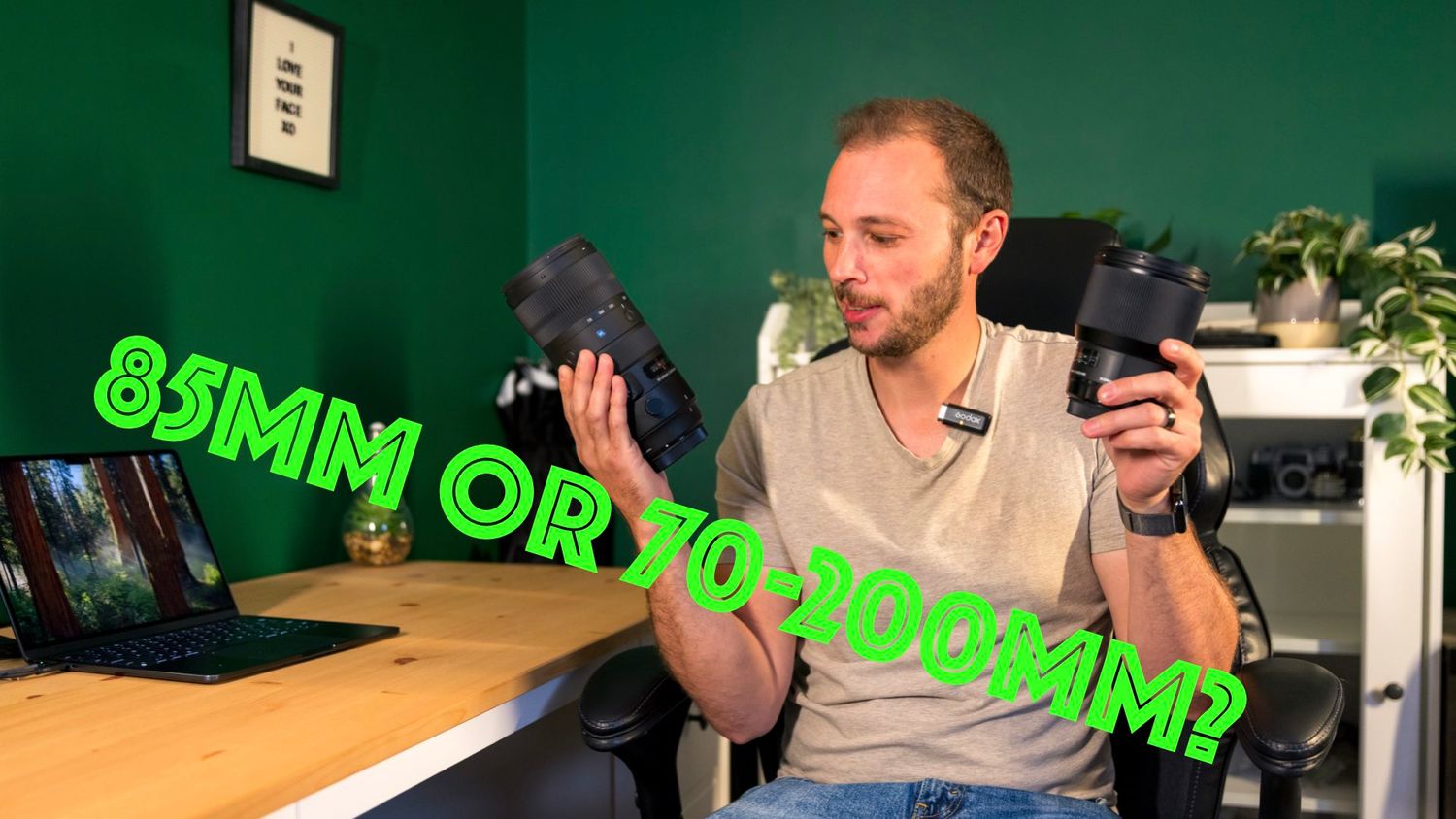 Tim Gowling holds up two camera lenses while sitting at a desk with text overlay reading '85MM OR 70-200MM?' in green neon style.