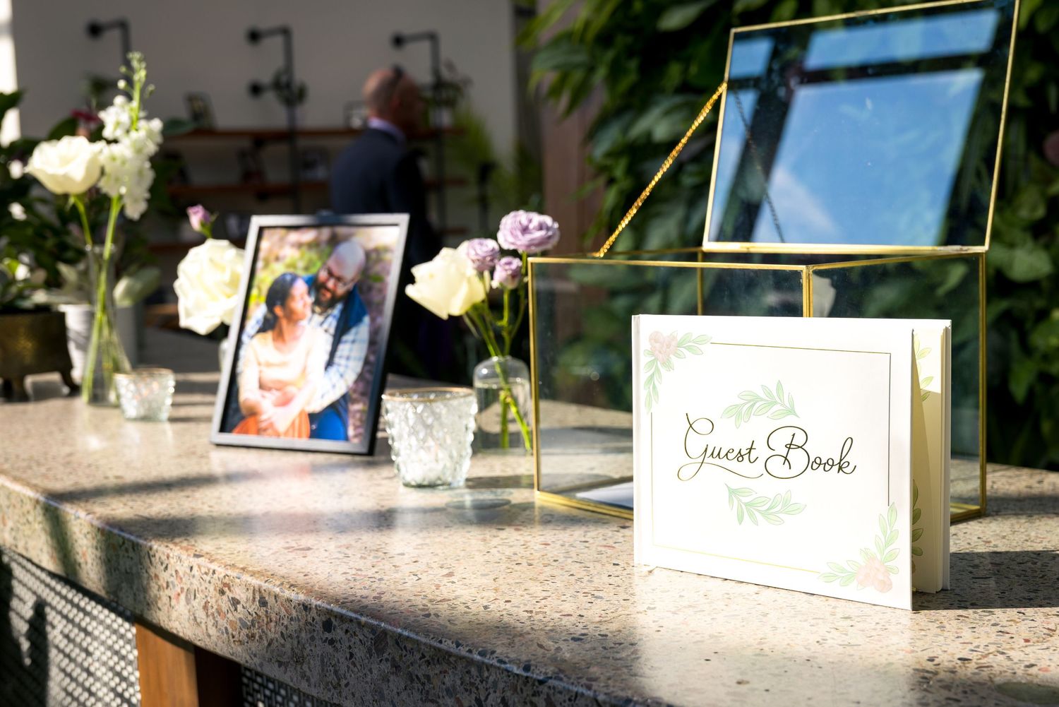 Guest book and framed photos displayed on stone counter with delicate flower arrangements and candlelight holders. Tim Gowling Photography