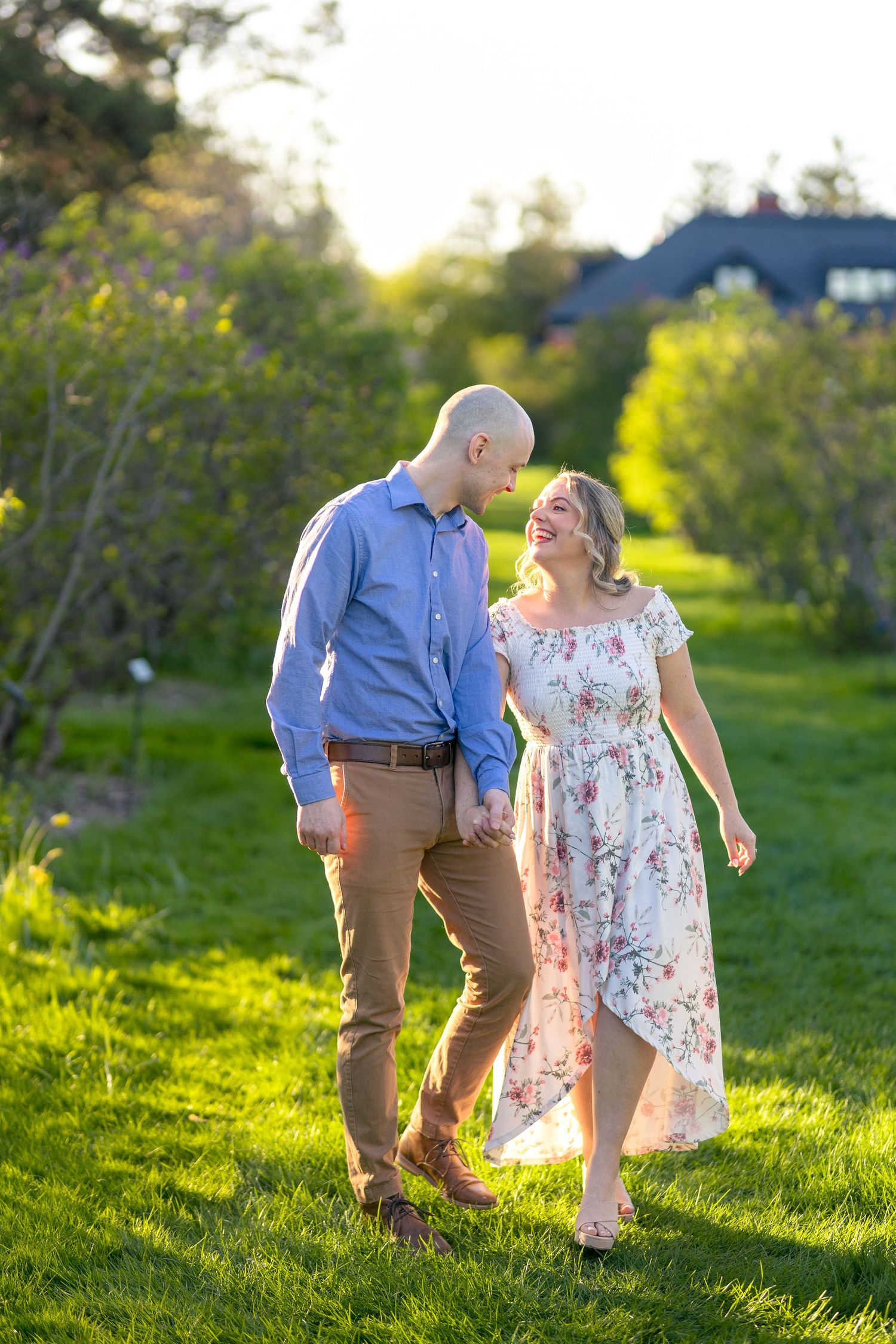 Couple walking together through sunlit meadow with flowering trees in background. Ottawa Wedding Photographer