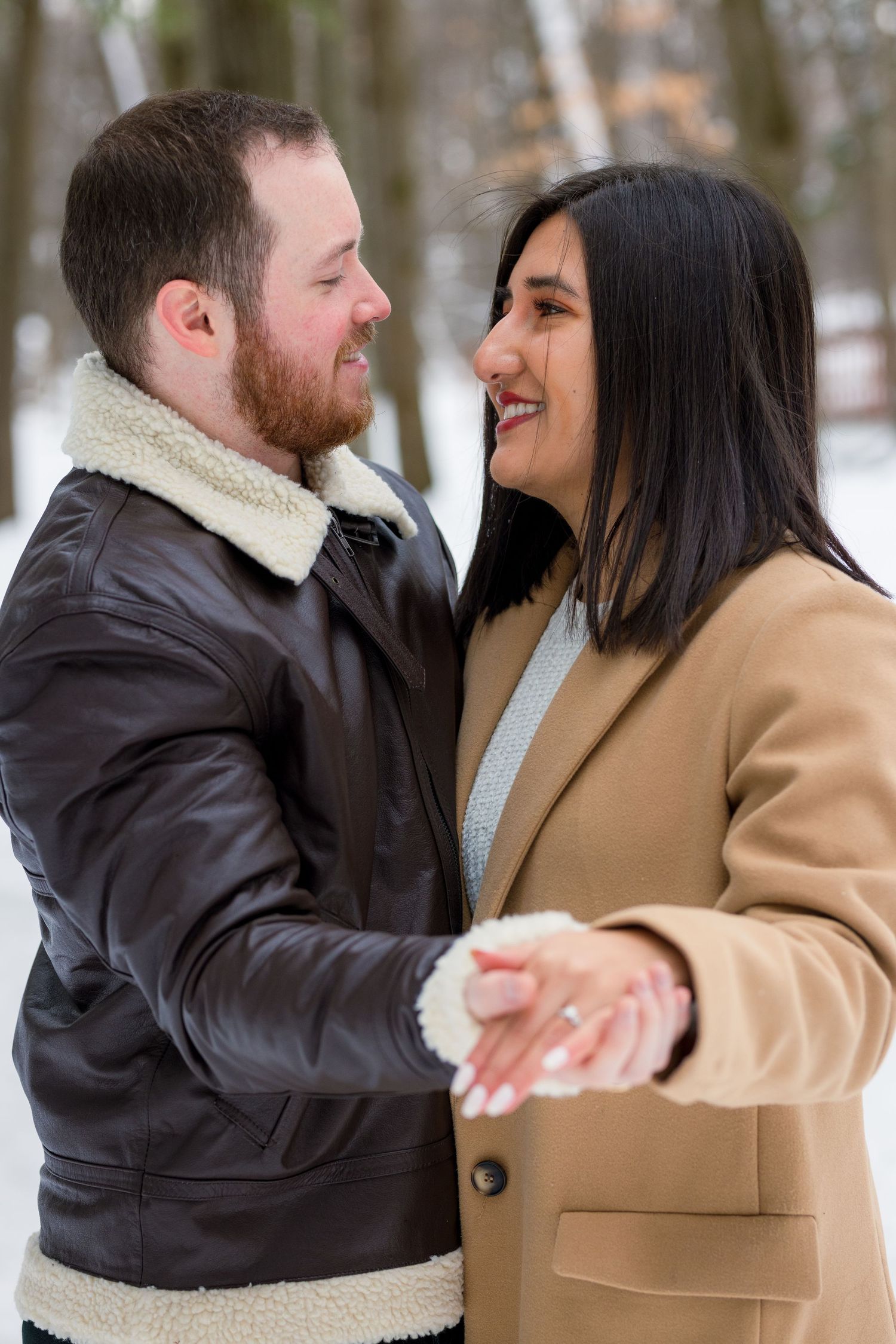 The couple sharing a joyful laugh as they stand together in the snow, wrapped in cozy winter coats.