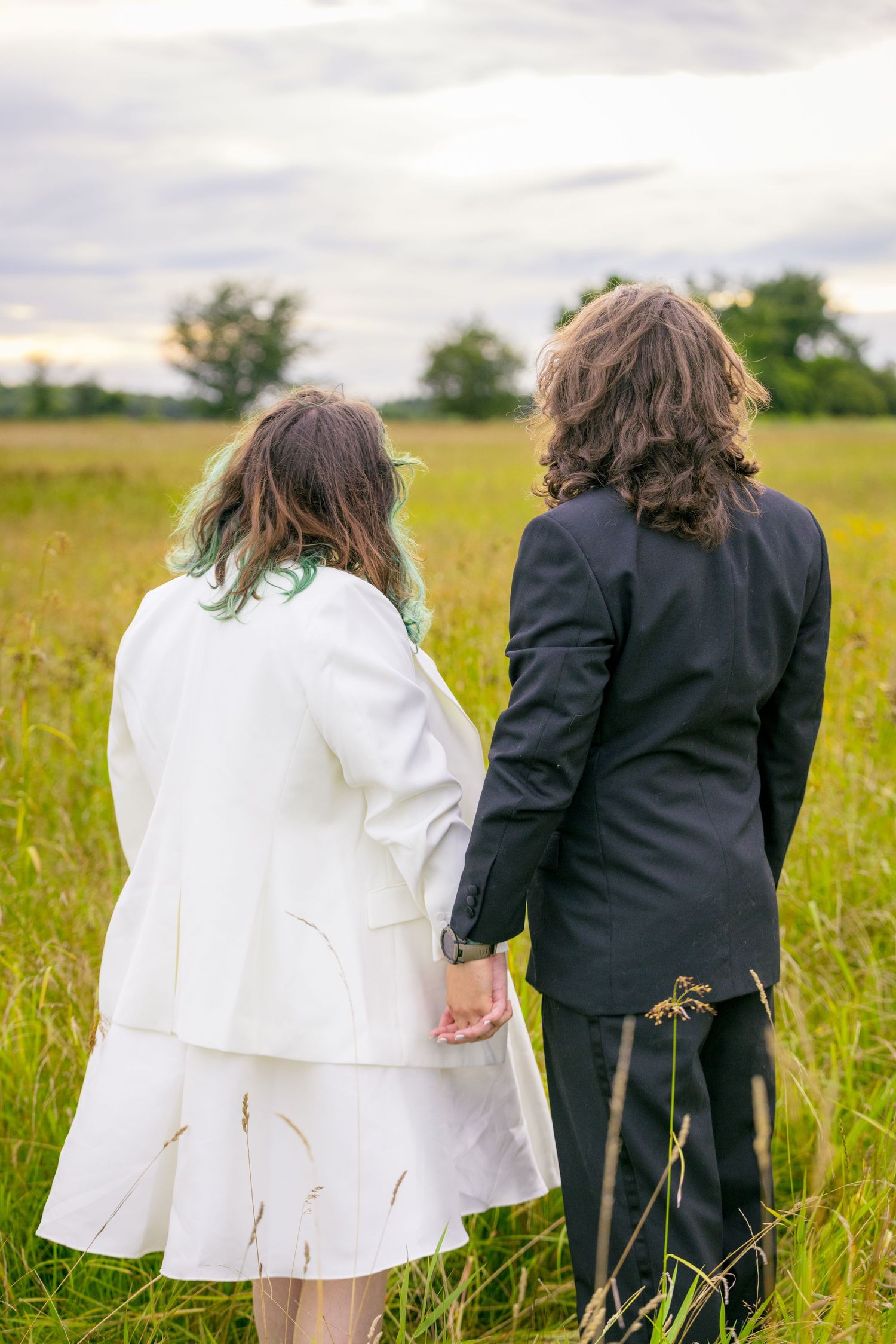 A couple in wedding attire stands together in a golden field under cloudy skies. Ottawa Wedding Photographer