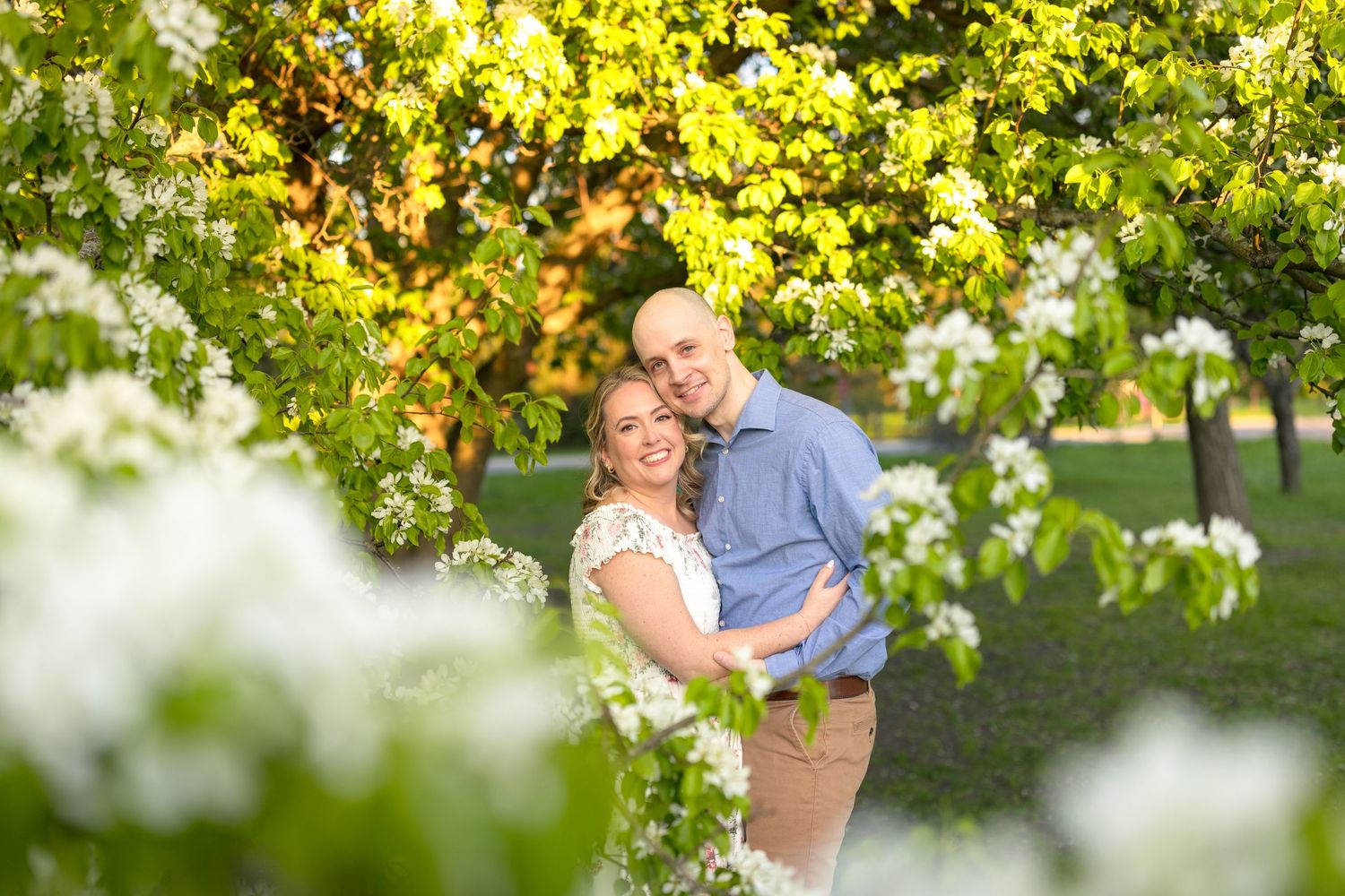 A couple shares a tender moment among white spring blossoms and green foliage. Ottawa Wedding Photographer
