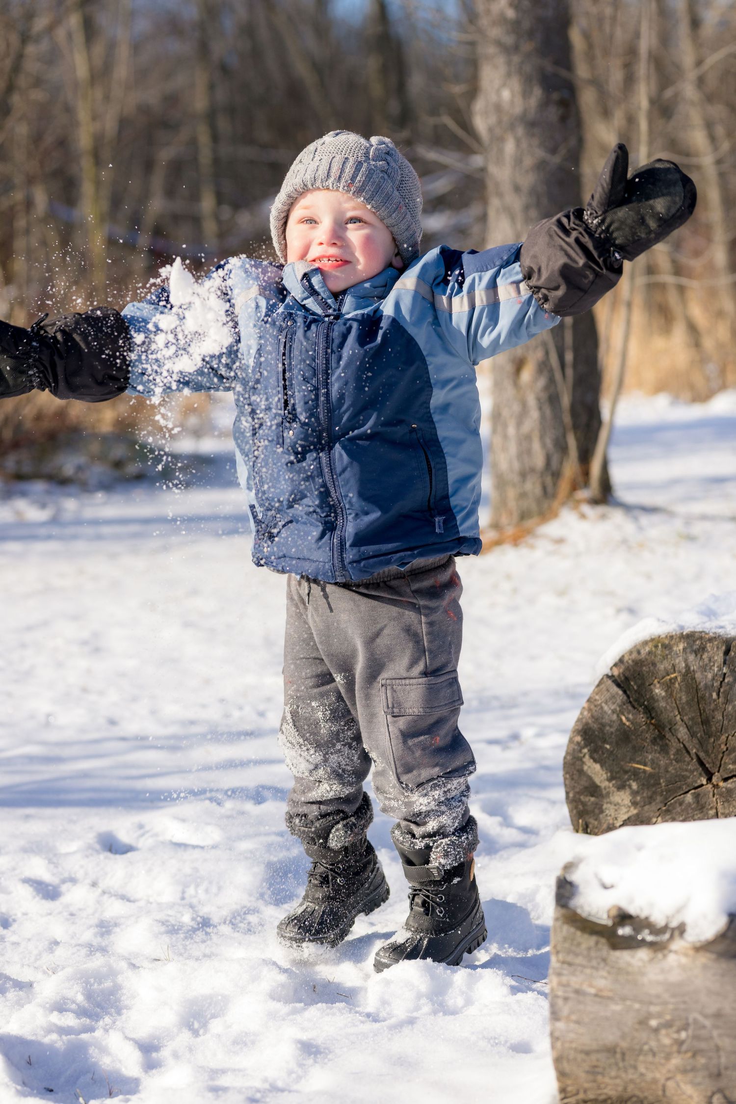 A small child in winter clothing plays and jumps in fresh snow near rocks. Ottawa Family Photographer