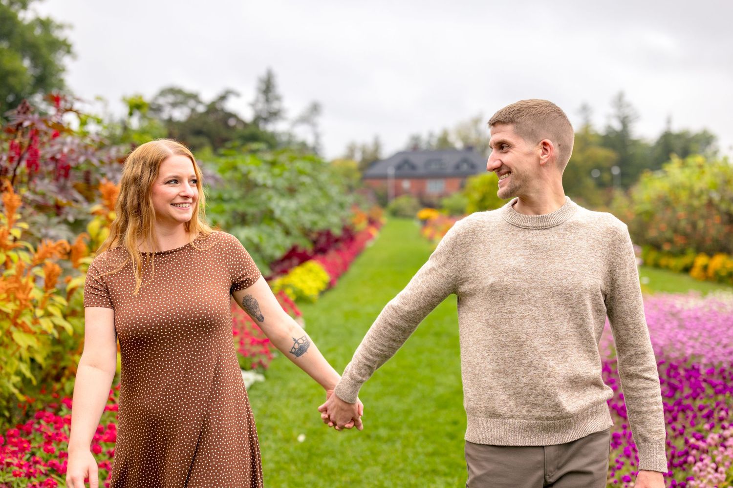 A couple holds hands while walking through a colorful garden filled with autumn blooms. Ottawa Wedding Photographer