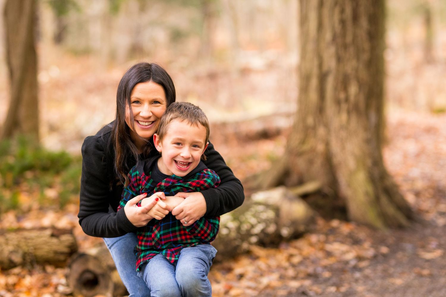 Two people sharing a warm embrace and laughing together in an autumn forest setting with fallen leaves.