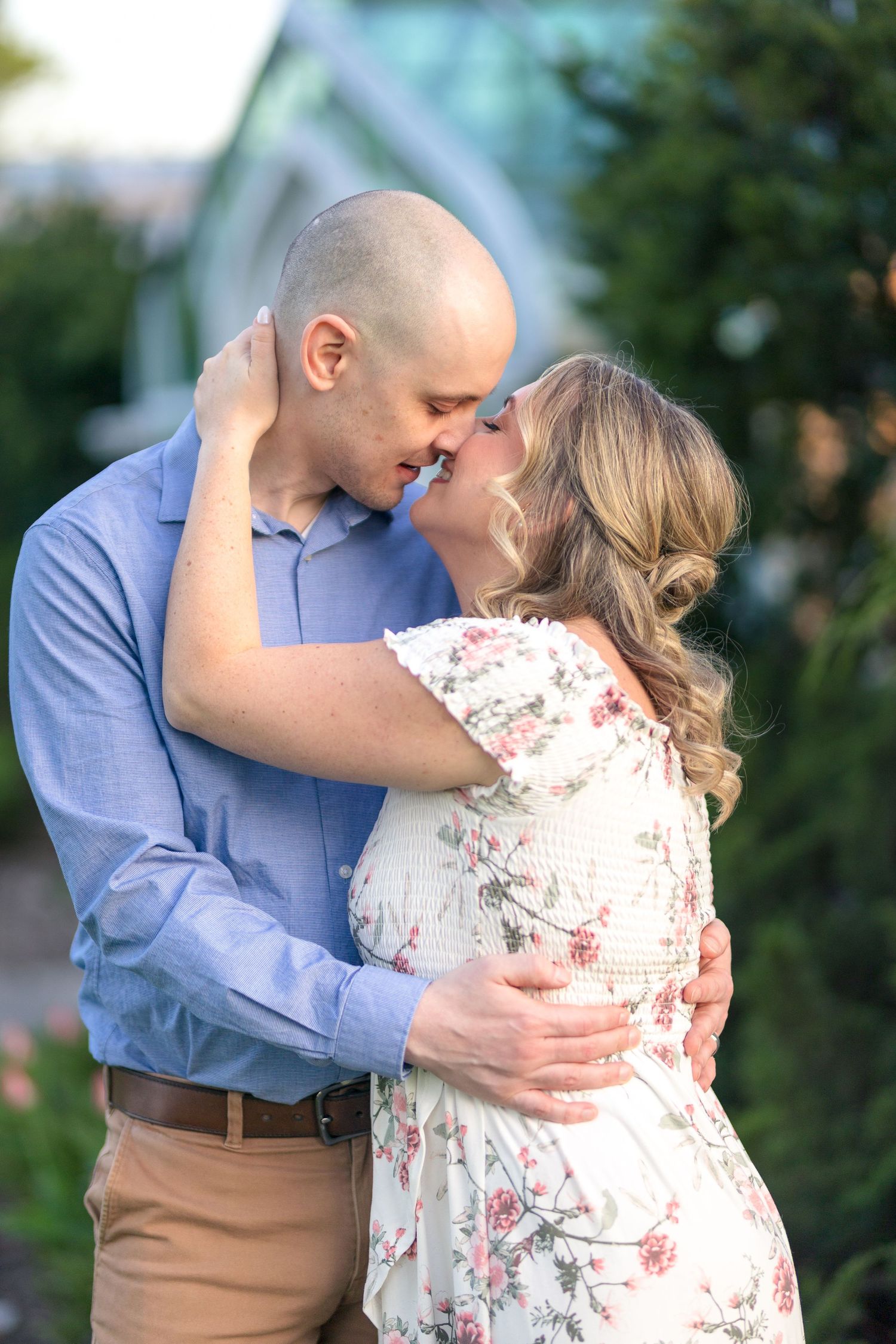 Romantic couple embracing in a garden setting wearing blue shirt and floral dress. Ottawa Wedding Photographer