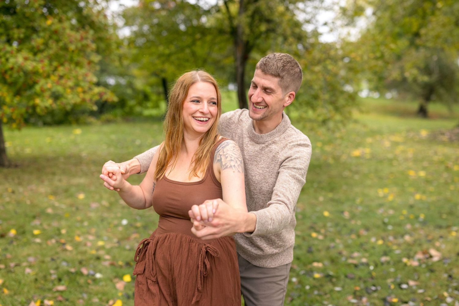 A couple dances together on grass with autumn trees in the background. Ottawa Wedding Photographer