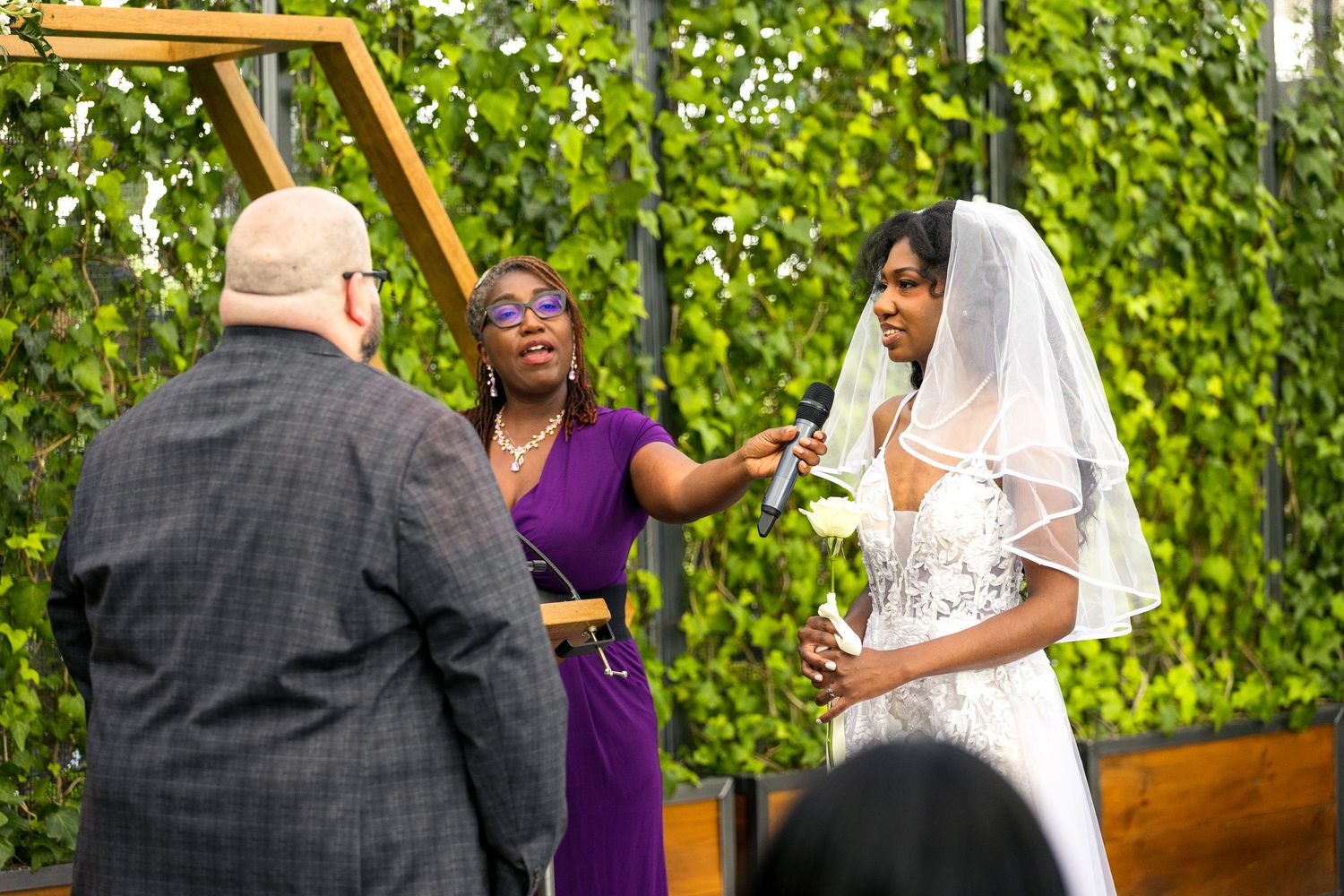 A joyful greenhouse wedding ceremony takes place in front of an ivy-covered wall with bright natural lighting. Tim Gowling Photography
