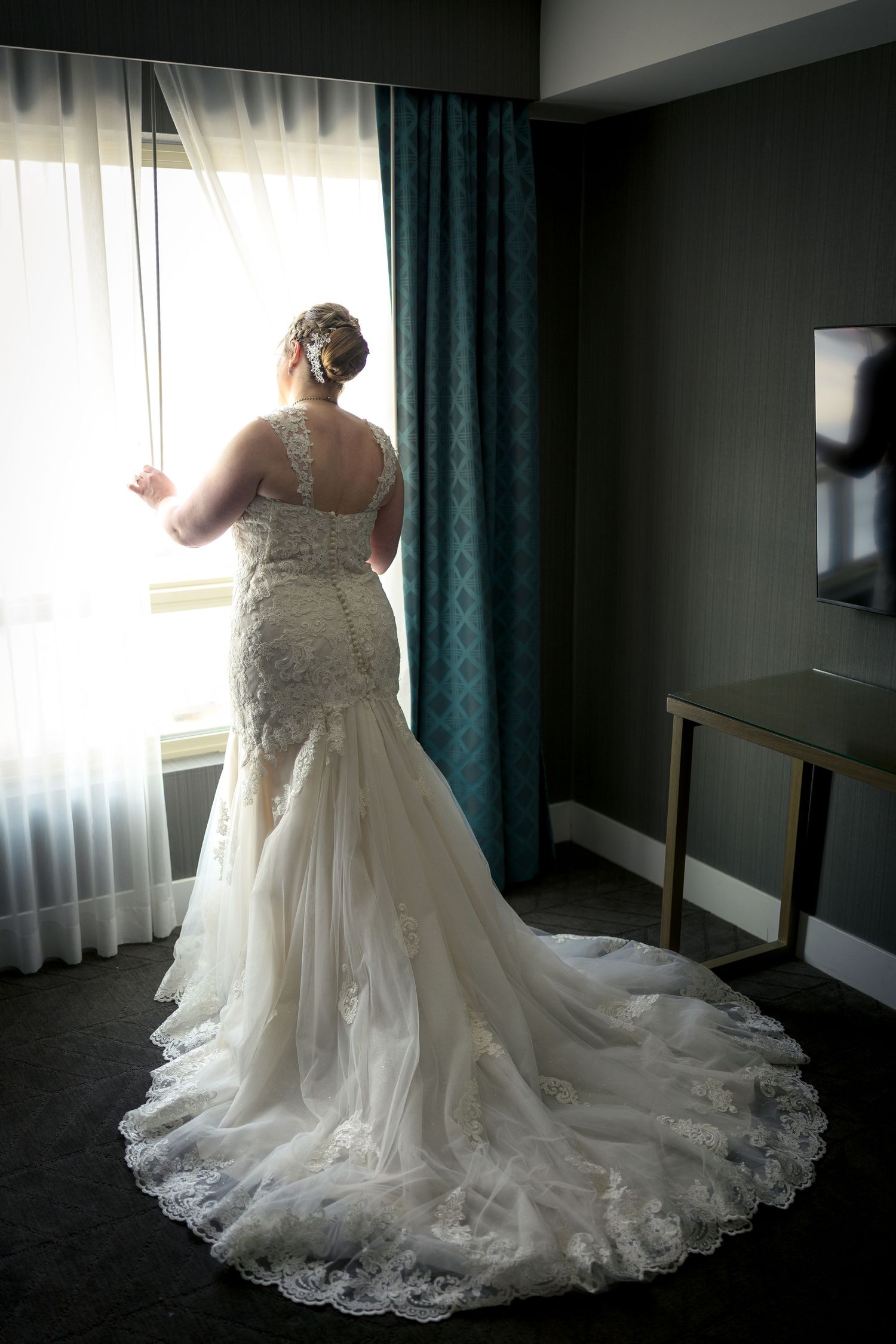 A wedding dress with delicate lace details and a flowing train is showcased in a hotel room . Ottawa wedding photographer