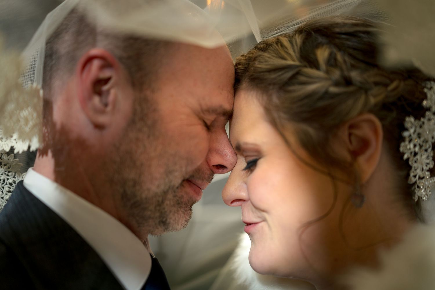A wedding couple share an intimate moment in a romantic scene with soft lighting under a veil. Ottawa Wedding Photographer