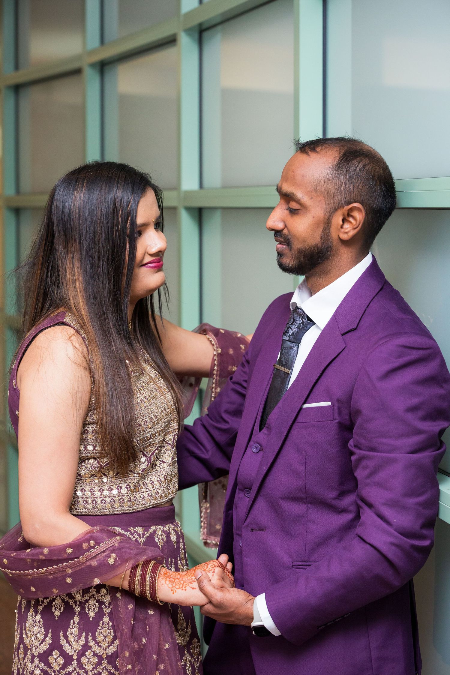 A couple in formal wear shares an intimate moment, with purple suit and gold embellished dress.