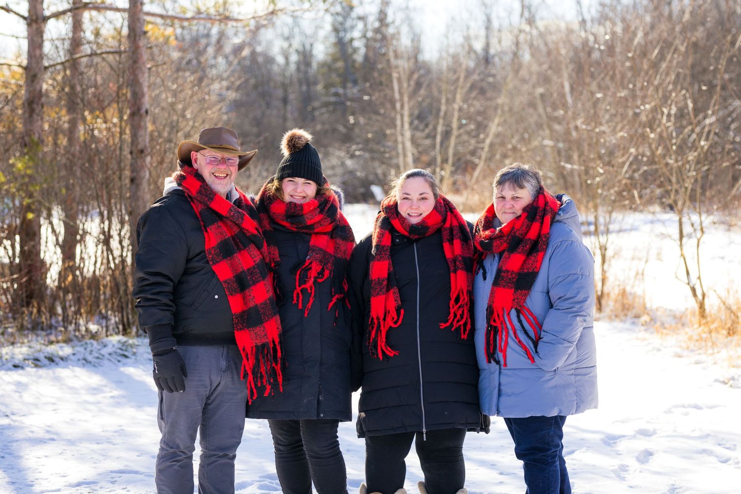 Group in matching red and black buffalo plaid scarves pose together on a snowy winter day.