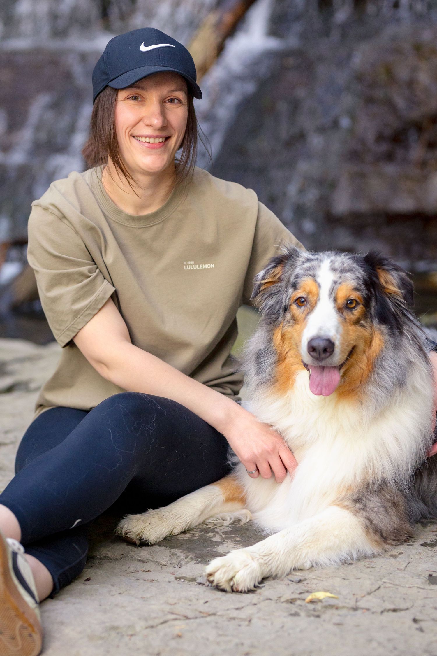 Australian Shepherd dog and companion sit together on rocky terrain near a waterfall. Ottawa Portrait Photographer