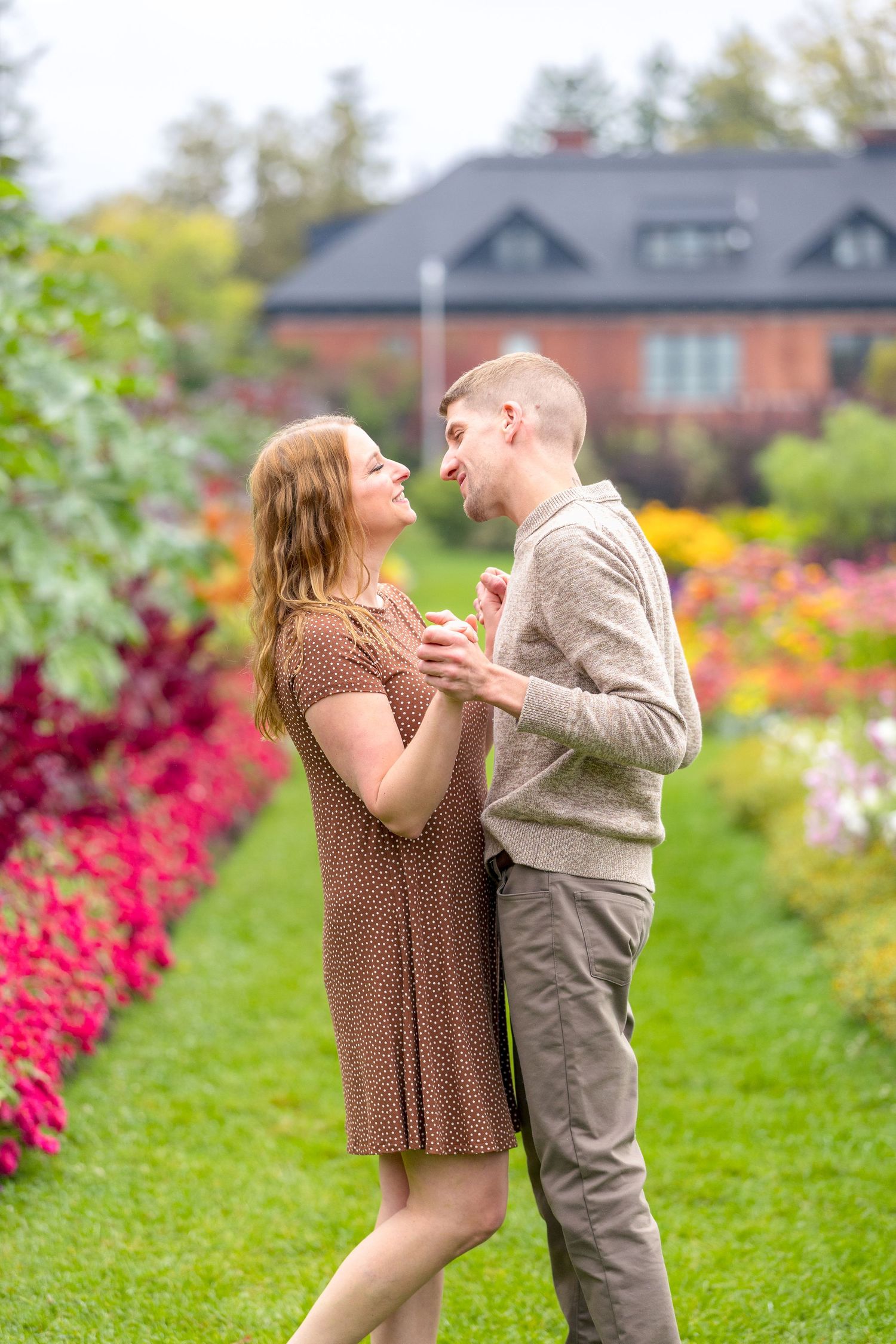 A couple shares an intimate moment in a garden with colorful flowers and a brick house in the background. Ottawa Wedding Photographer