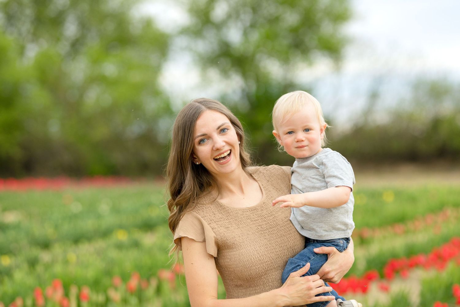 A mother and child walk together through a field of vibrant red tulips on a sunny spring day. Ottawa Portrait Photographer
