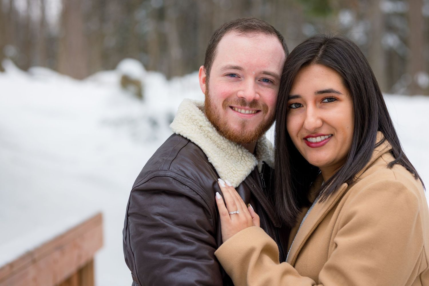 A newly engaged couple embracing, with the snow gently falling around them, creating a magical winter atmosphere.