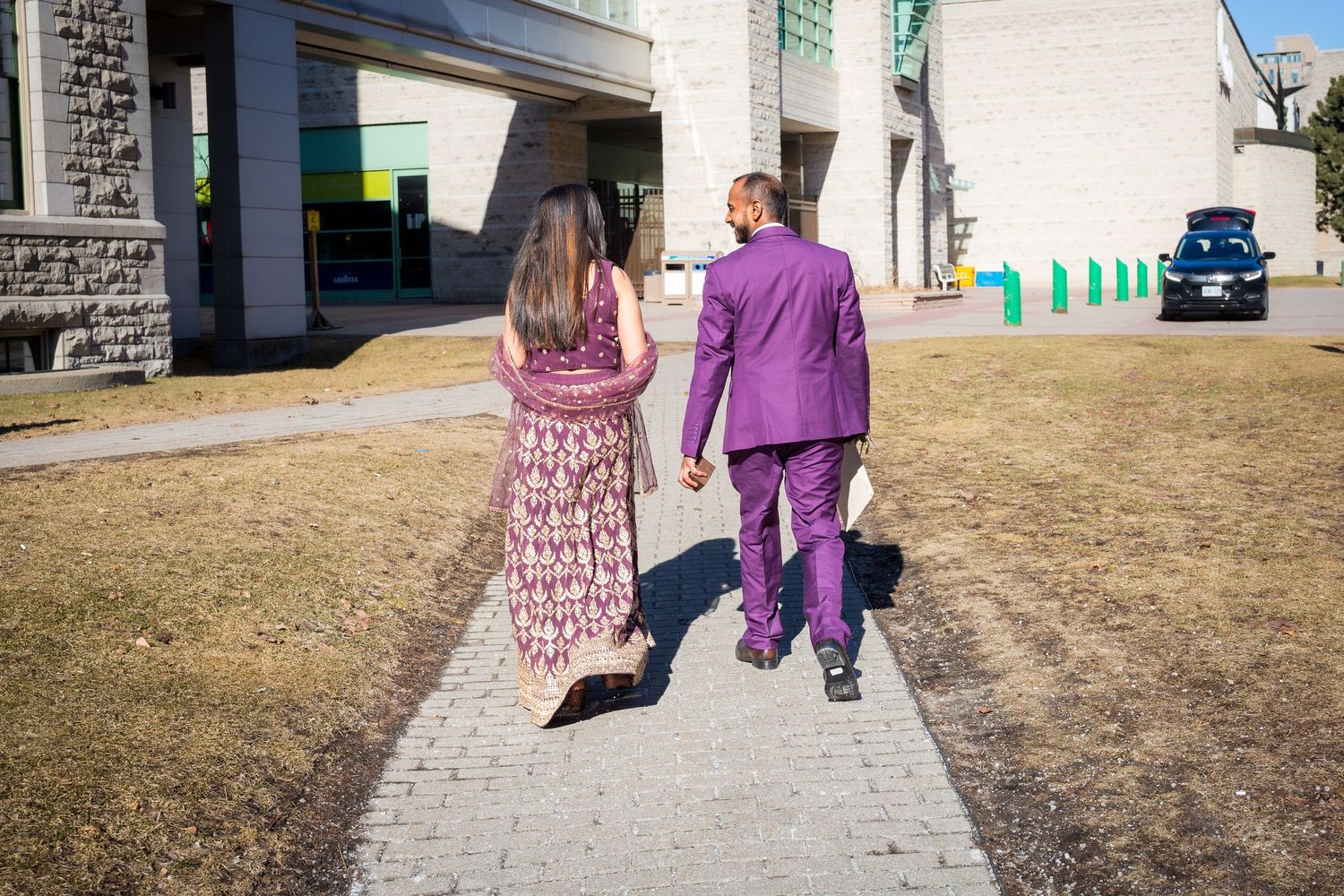 Two people walking on a sidewalk wearing coordinated purple and burgundy outfits.