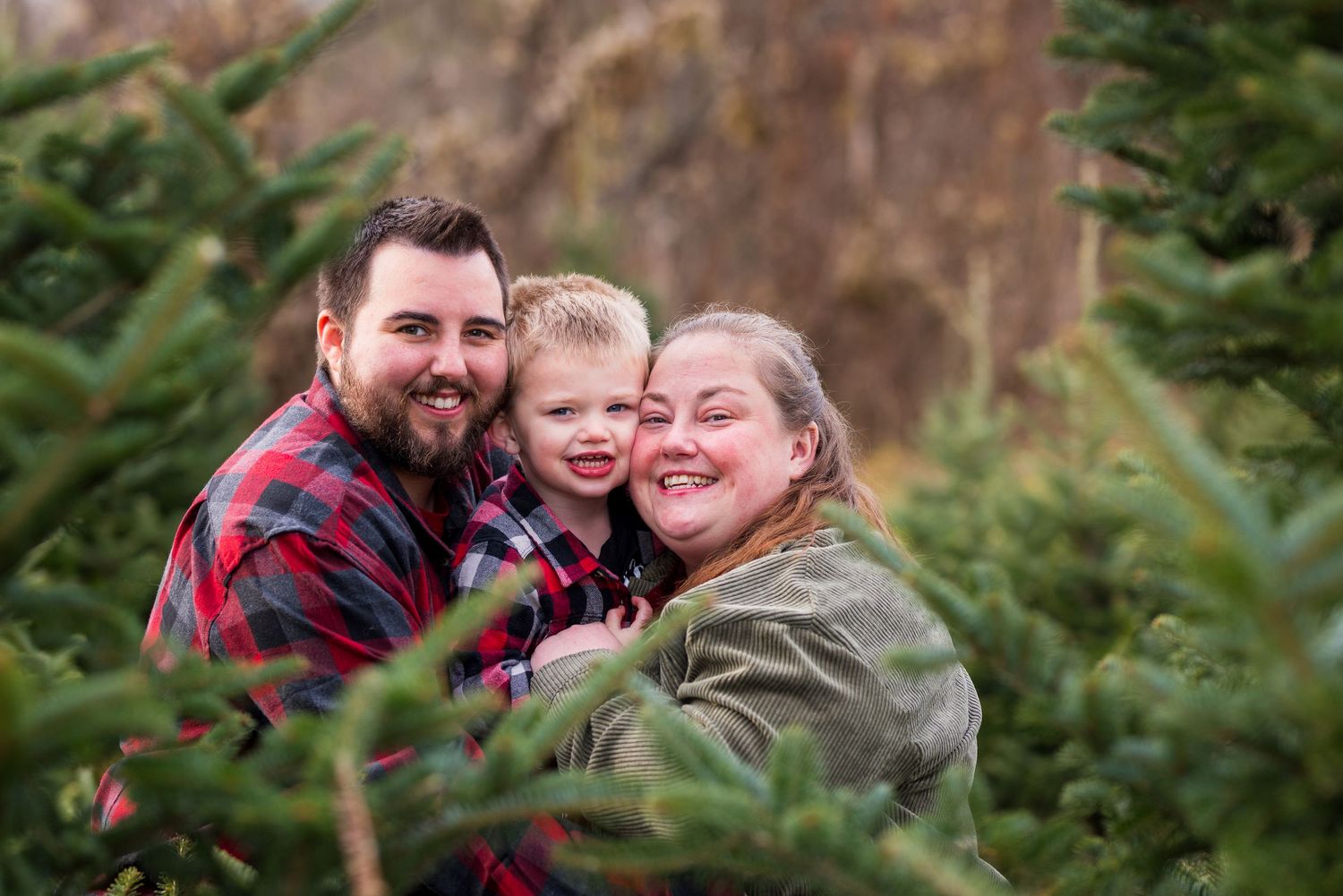 A family shares a joyful moment together while surrounded by evergreen Christmas trees in an outdoor setting. Ottawa Portrait Photographer