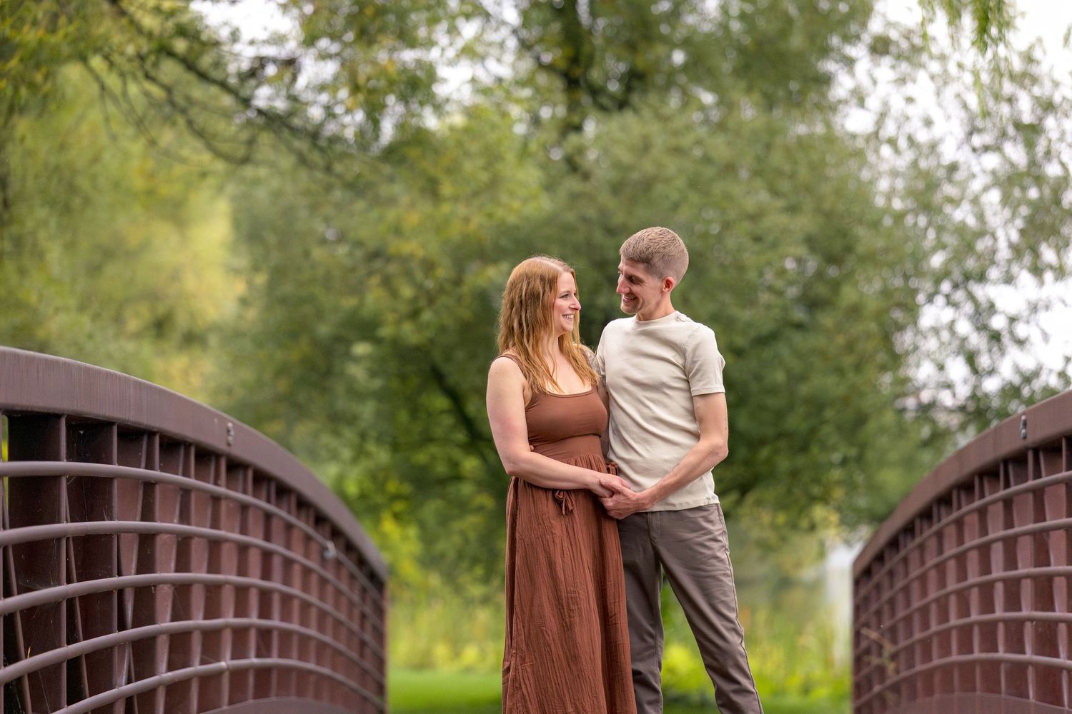 Romantic couple sharing tender moments on a wooden bridge surrounded by lush greenery. Ottawa Wedding Photographer