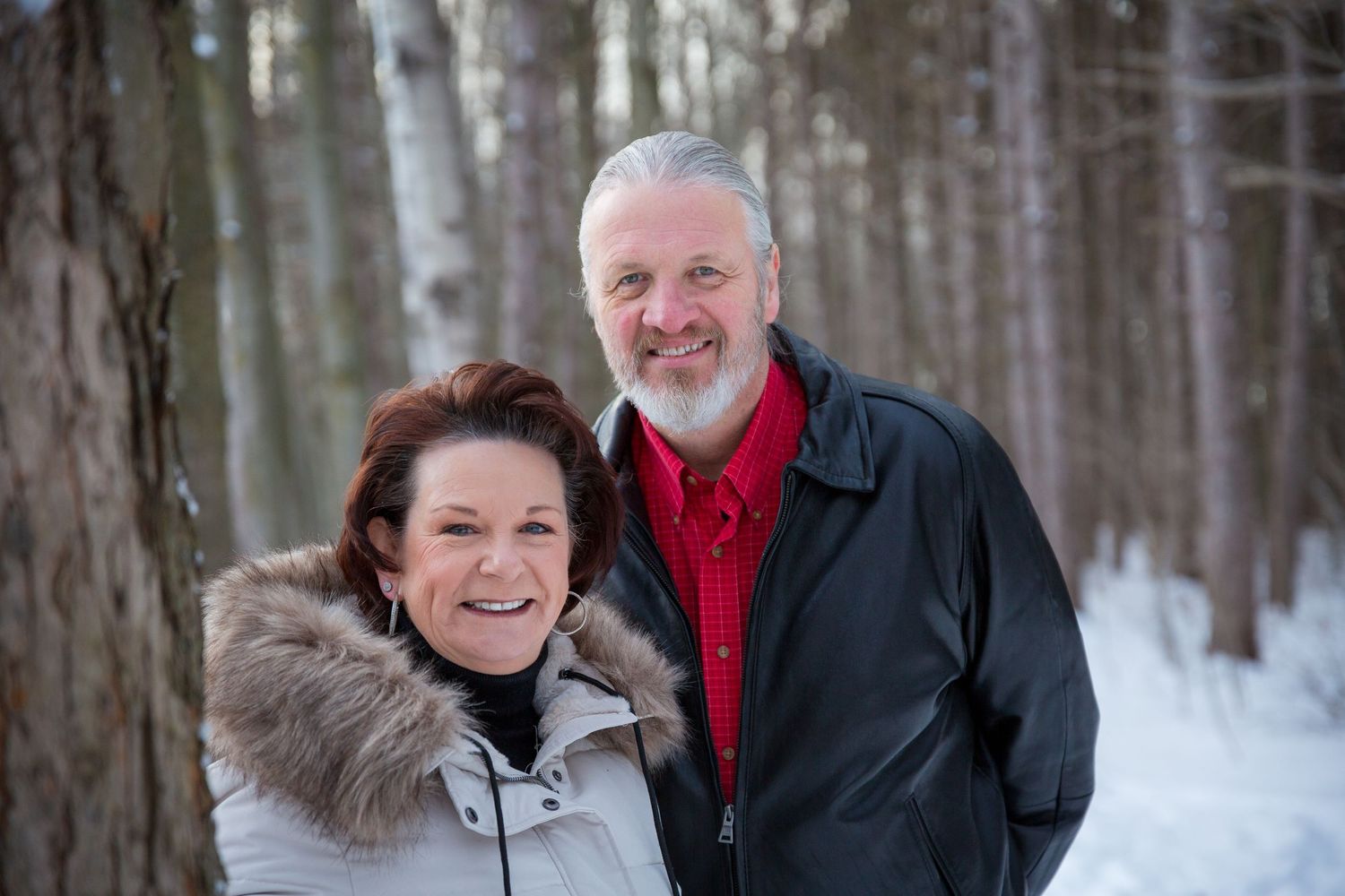 Smiling couple posing in a snowy forest with winter coats.