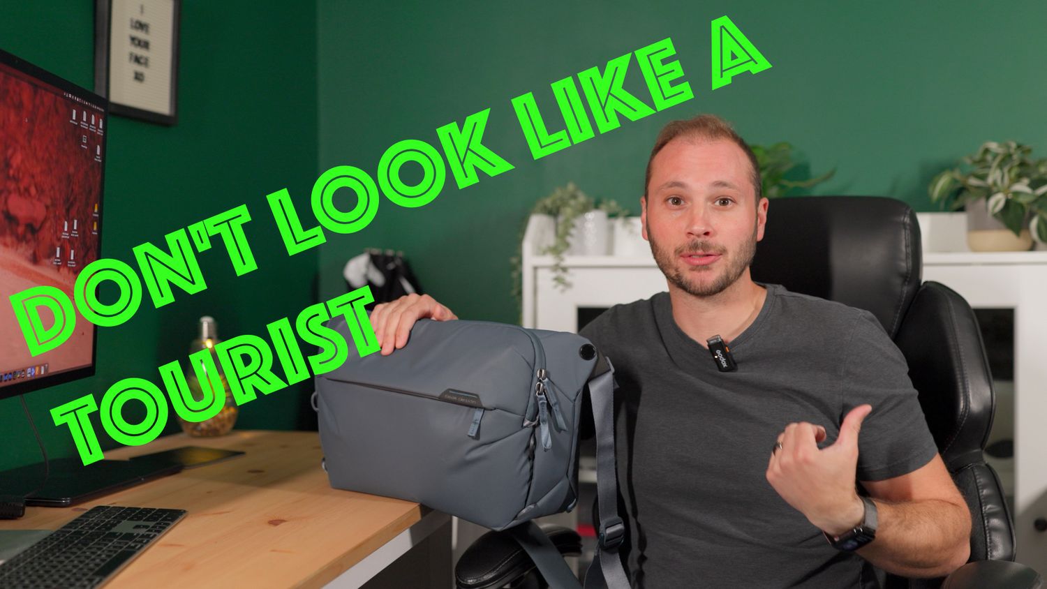 A man holds a gray Peak Design backpack with text reading Don't Look Like A Tourist in a home office setting.