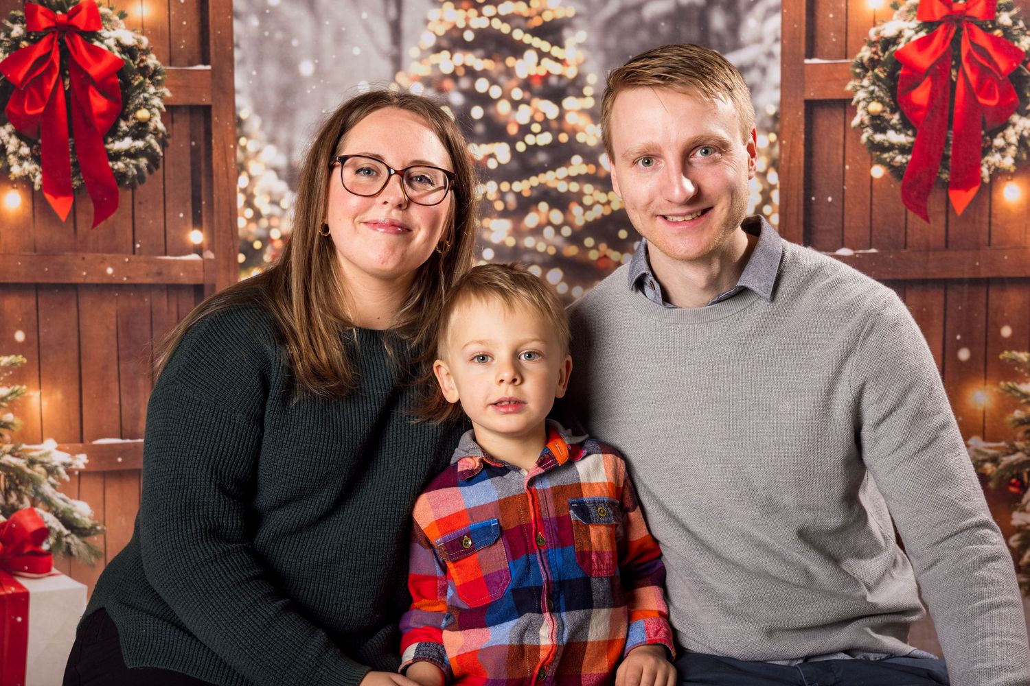 A family poses in front of a Christmas tree with red bows and festive holiday decorations in the background.