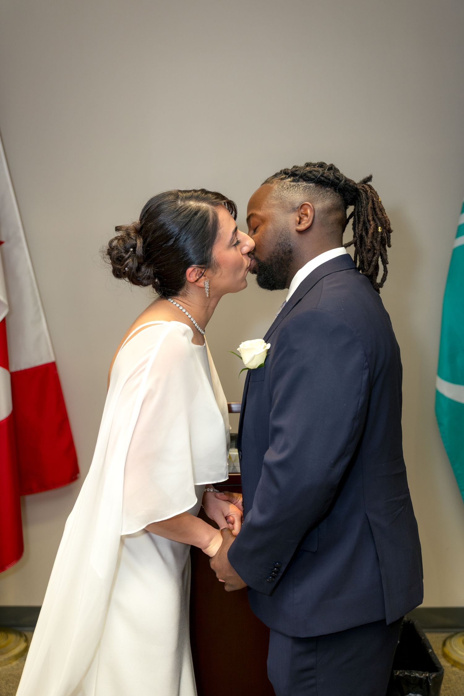 Interracial couple sharing first kiss at wedding ceremony, bride in white cape dress, groom in navy suit with dreadlocks. Ottawa Wedding