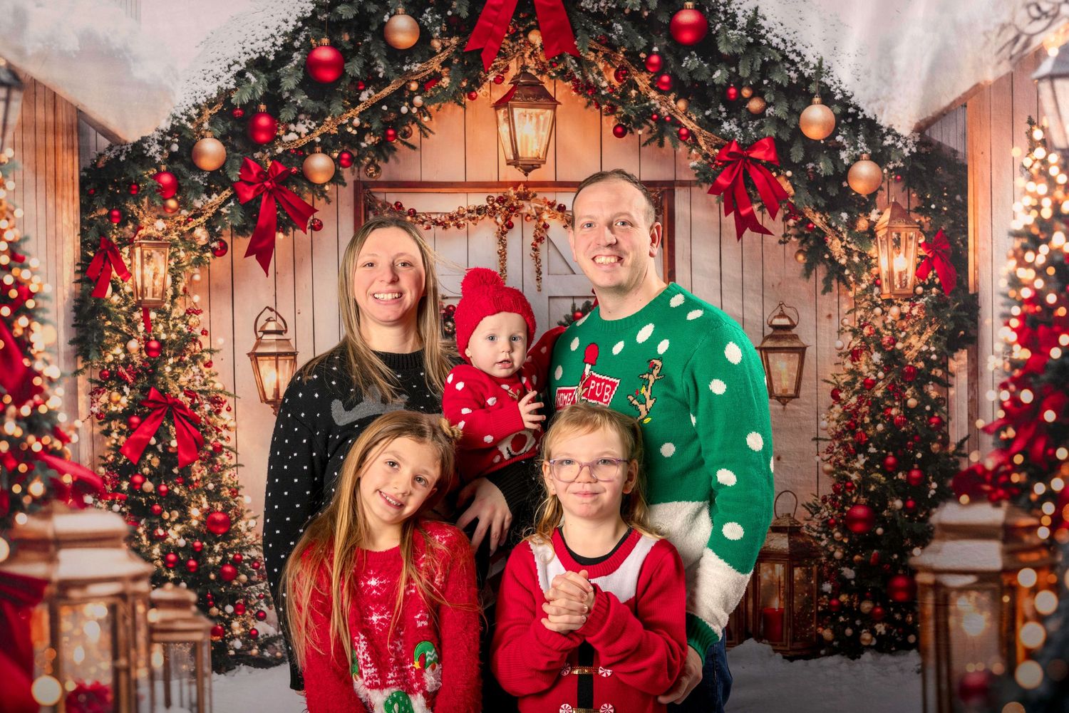 Family poses in festive holiday attire under decorated Christmas arch with twinkling lights. Ottawa Family Photographer