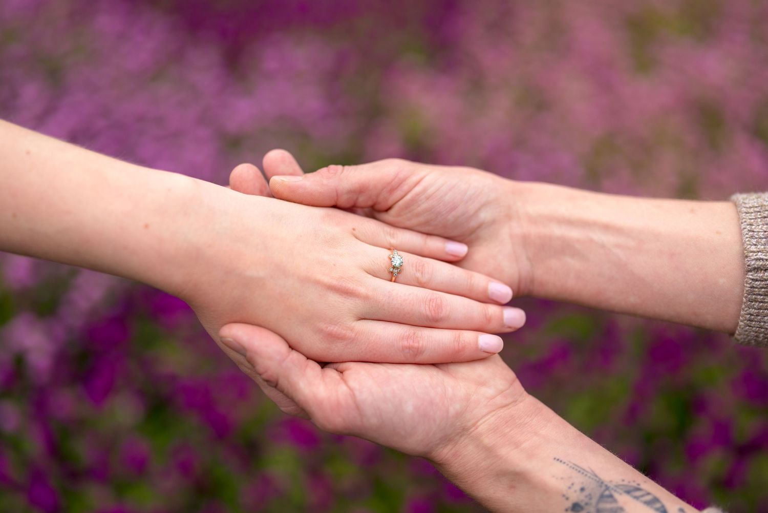 Close-up of hands with an engagement ring against purple flowers in a garden setting. Ottawa Wedding Photographer