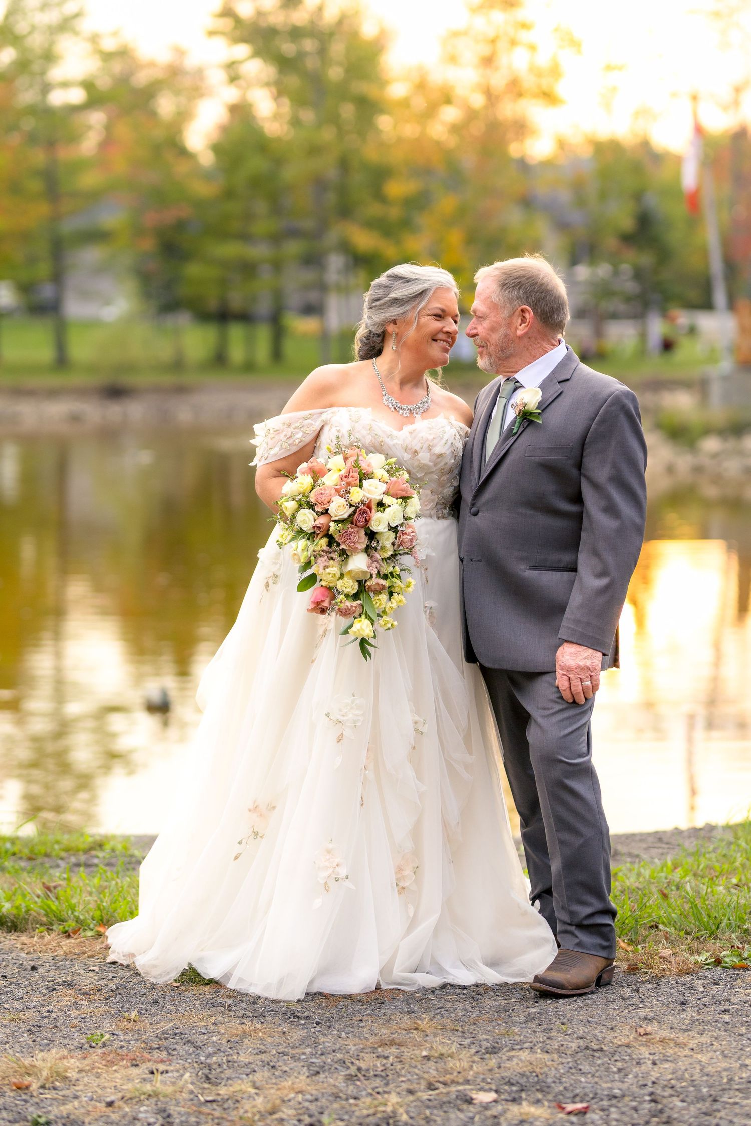 A romantic wedding couple poses by a lake at sunset having thier photos showing their special day. Ottawa wedding photographer