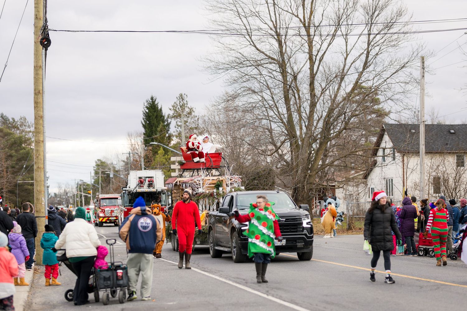 Santa Claus waves from a parade float during a small town holiday celebration with spectators lining the street.
