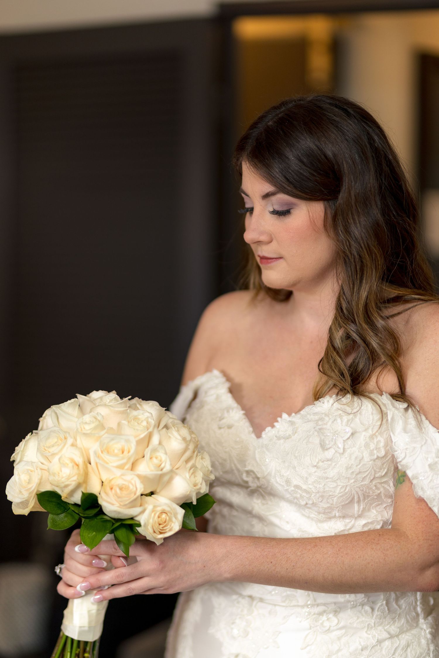 A bride in a white lace wedding dress holds a bouquet of cream roses while posing for elegant bridal portraits. Ottawa Wedding Photographer