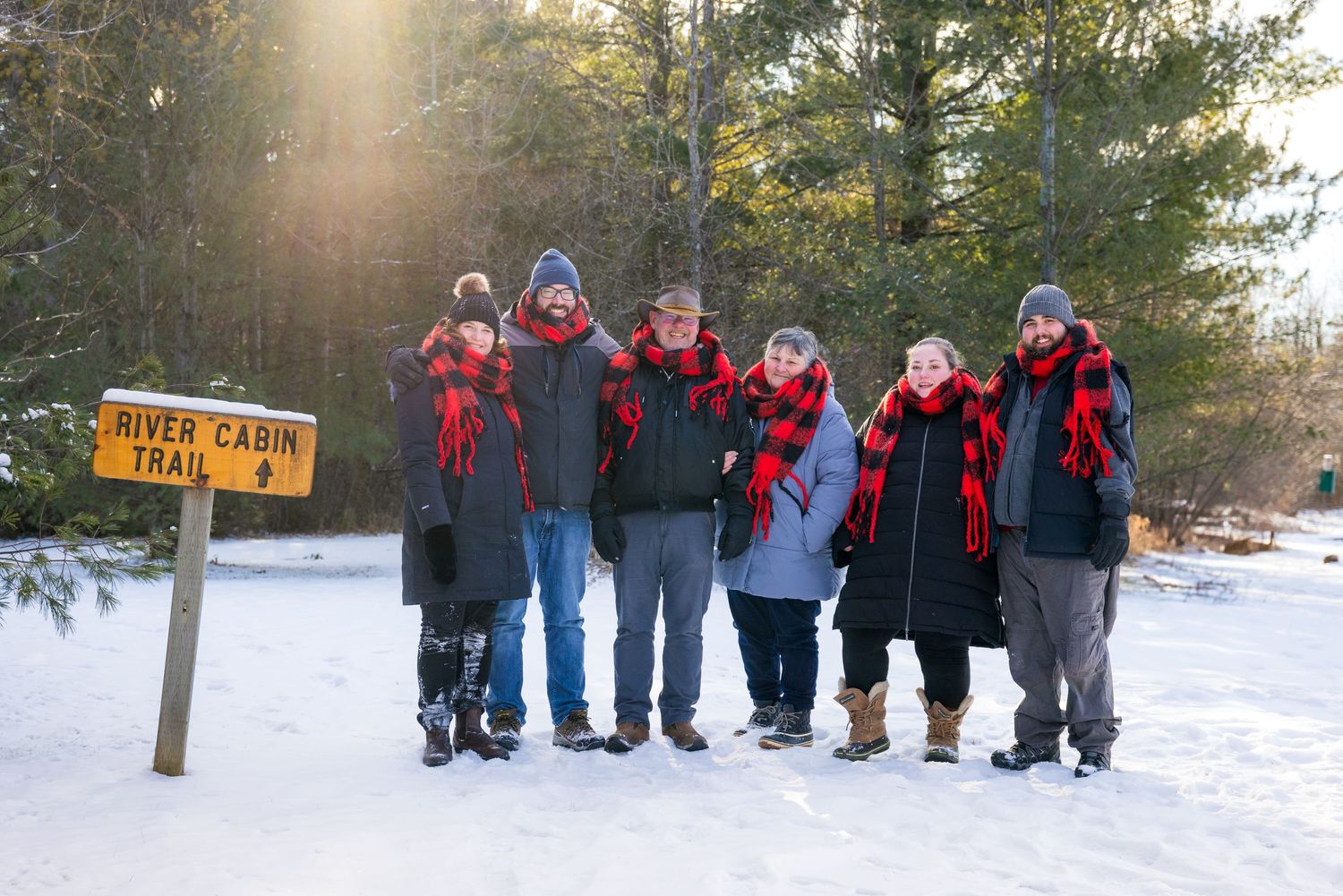 A group shot of the entire family, gathered closely and smiling against the beautiful backdrop of a snowy conservation area.