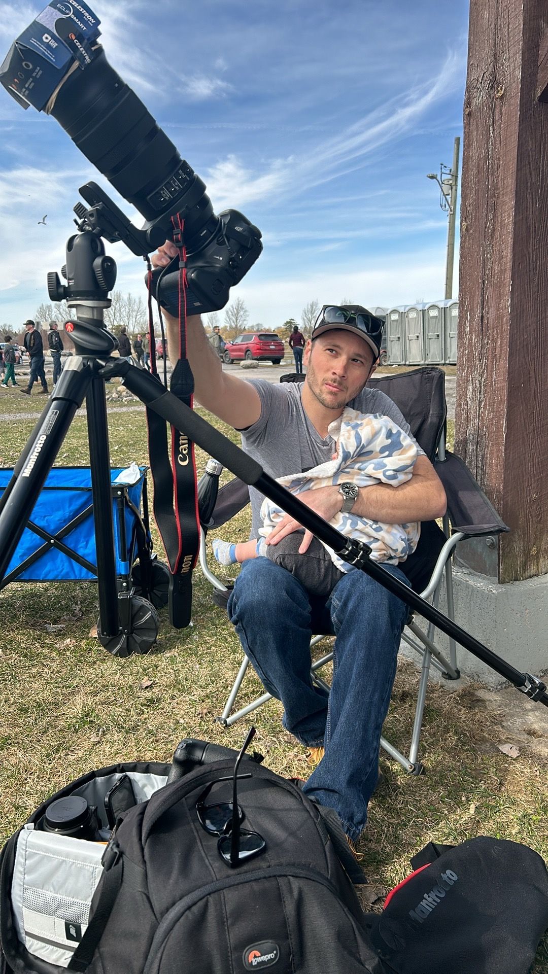 Photographer sitting with camera equipment and tripod setup outdoors.