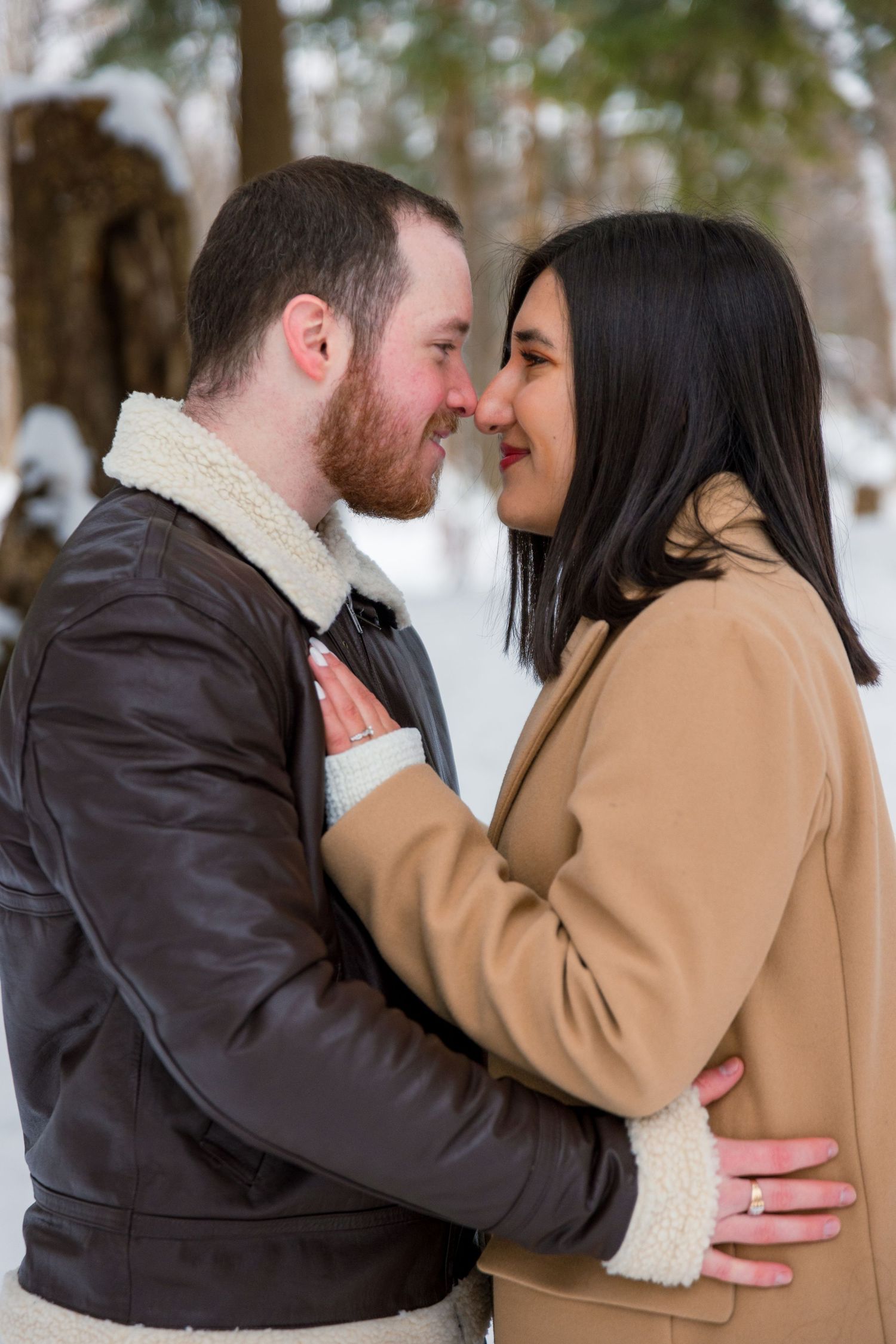 A newly engaged couple embracing, with the snow gently falling around them, creating a magical winter atmosphere.
