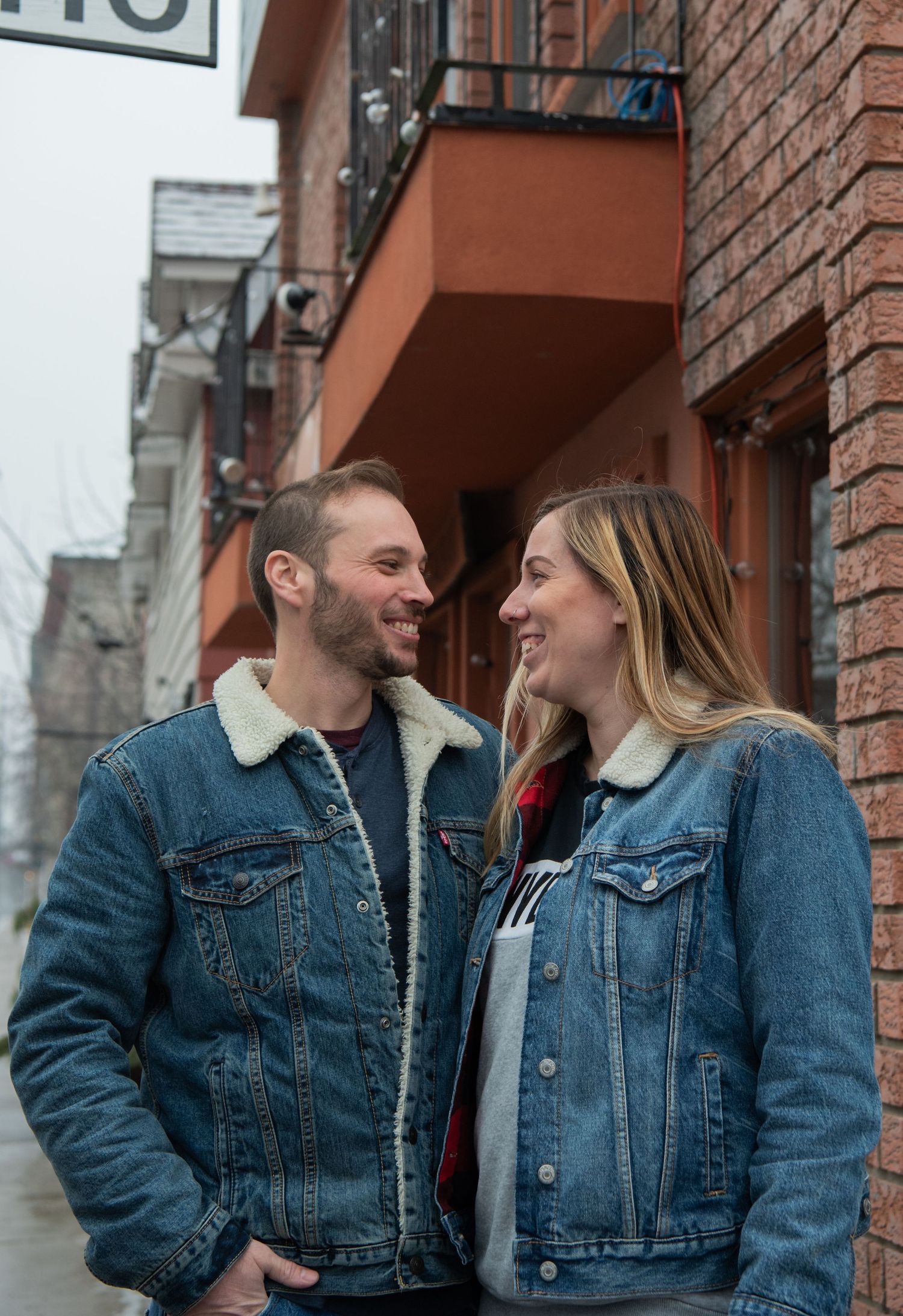 Ottawa wedding & lifestyle photographer & his wife have matching denim jackets share intimate moments against a brick wall on a city street.