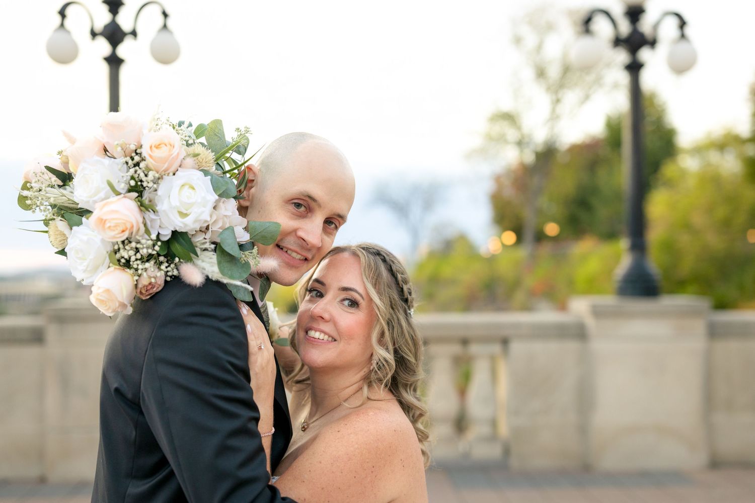 A wedding couple poses together on a stone terrace at the Fairmont Château Laurier with fall trees. Ottawa Wedding Photographer