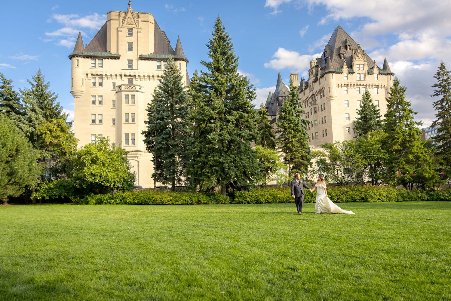The bride & Groom walk on the lawn behind the Fairmont Château Laurier having the formal photographs taken by Ottawa wedding photographer