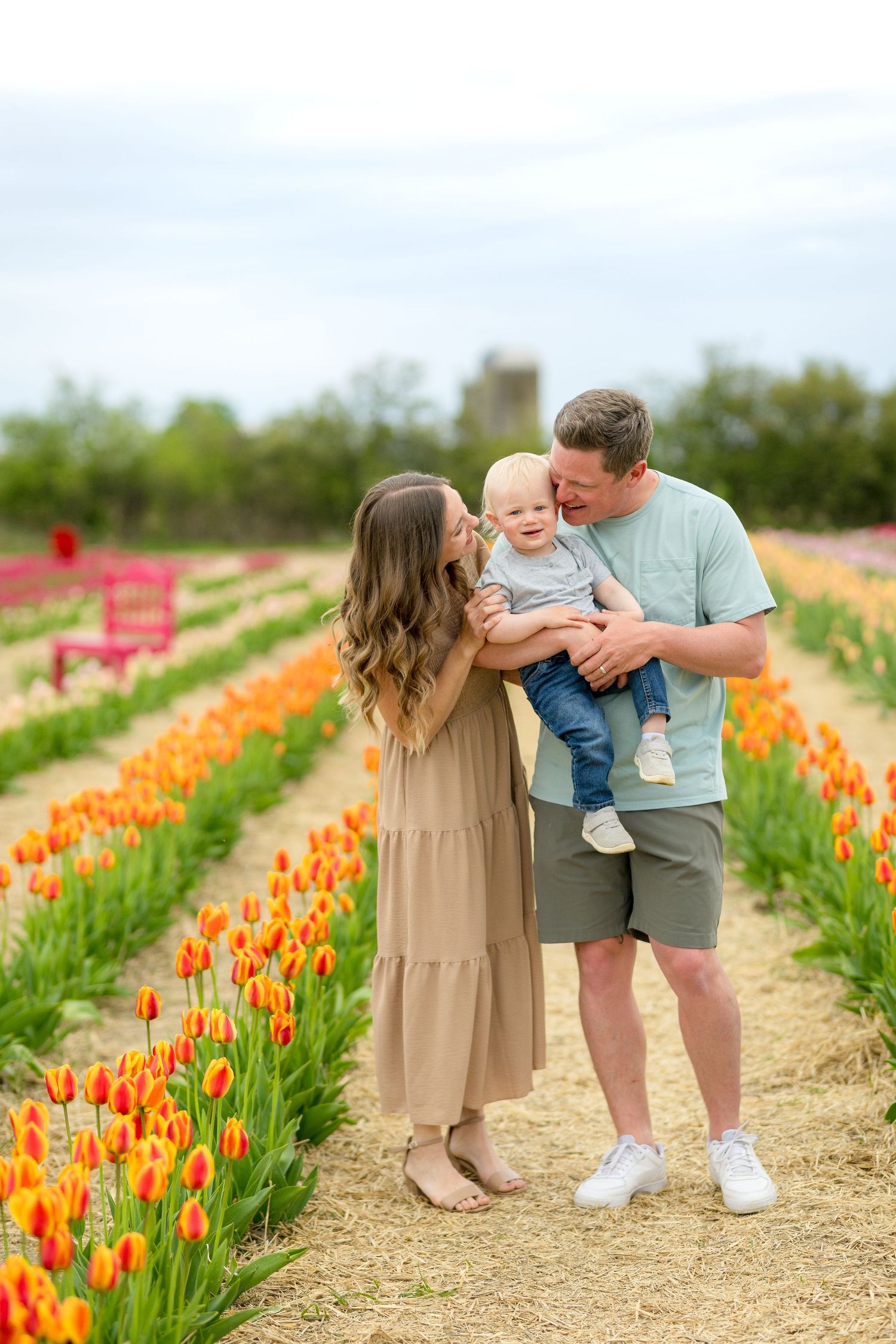 A family enjoys a spring day together while standing between rows of vibrant orange tulips in a flower field. Ottawa portrait photographer
