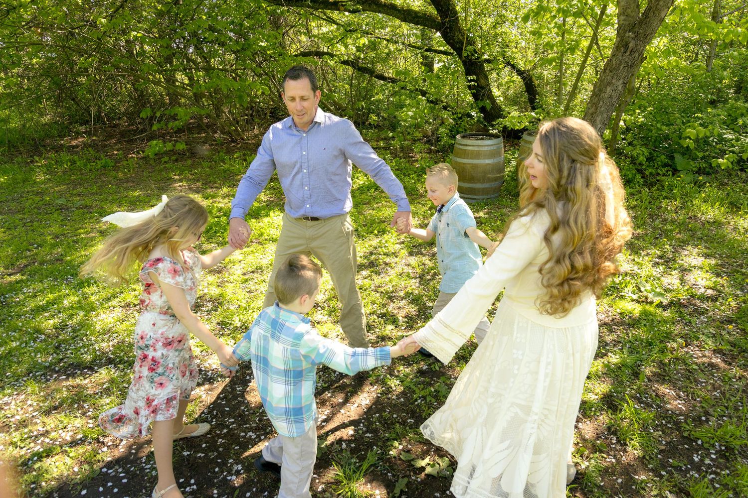 Family of five holding hands in a circle outdoors in a lush green park on a sunny day. Ottawa Family Photographer