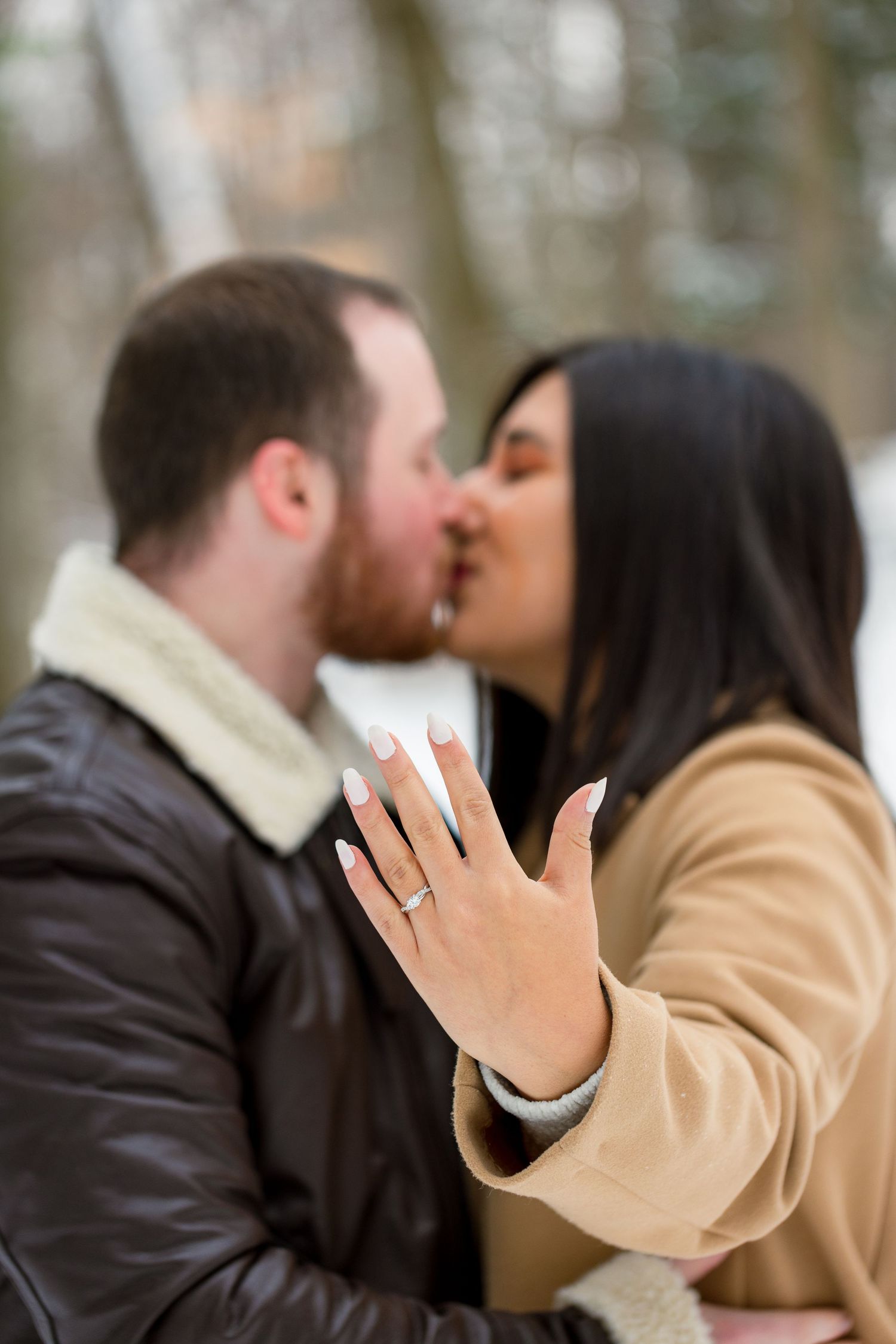 A sparkling engagement ring resting on the bride-to-be’s hand, surrounded by soft snow on a winter day.
